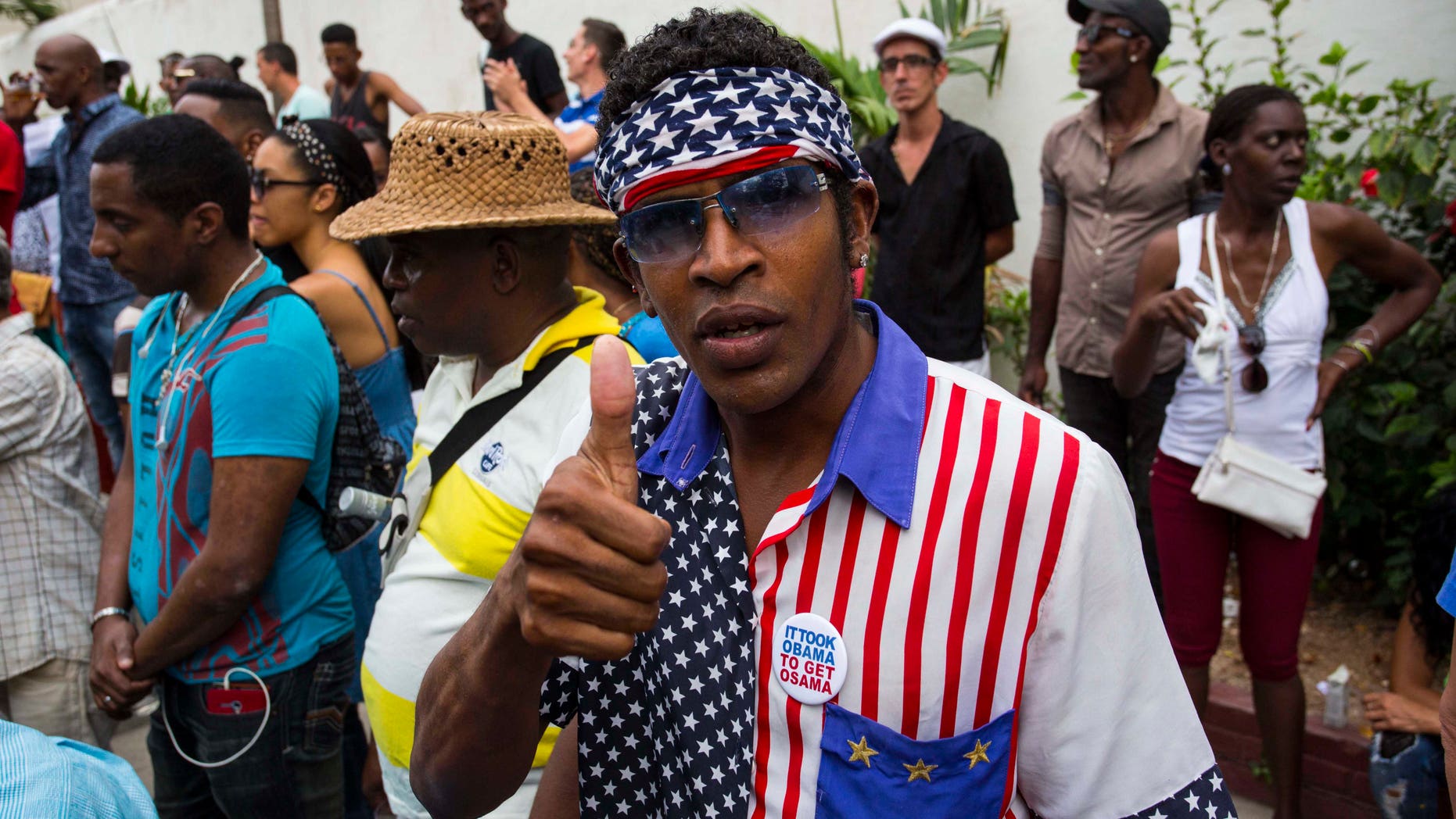 A man wearing a shirt and head scarf with a Stars and Stripes motif flashes a thumbs up at a weekly rumba dance gathering in Havana, Cuba, Saturday, March 19, 2016. President Barack Obama will travel to the communist island March 20. During his three-day trip, the first to the country by a sitting president in nearly 90 years he will meet with President Raul Castro at the Palace of the Revolution and attend a baseball exhibition game. (AP Photo/Desmond Boylan)