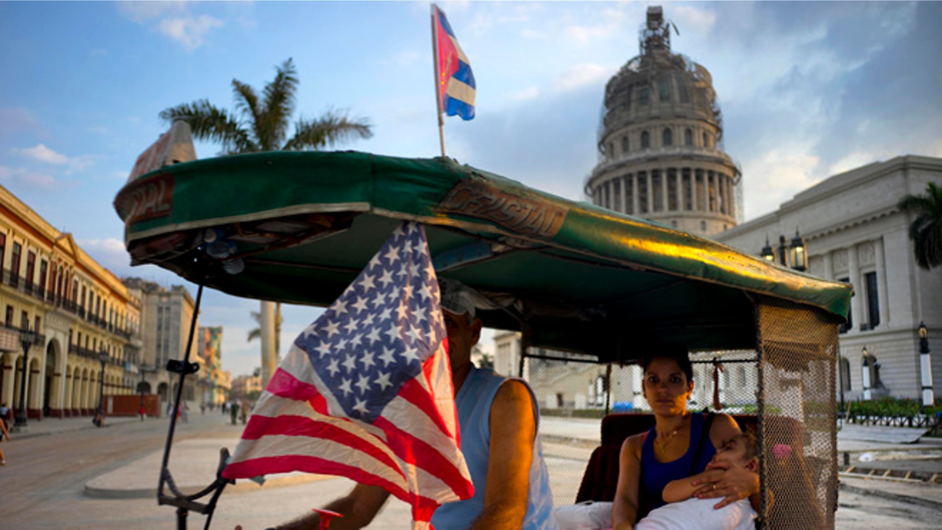 A taxi pedals his bicycle, decorated with Cuban and U.S. flags, as he transports a woman holding a sleeping girl, near the Capitolio in Havana, Cuba, Tuesday, March 15, 2016. President Barack Obama will travel to Cuba on March 20. (AP Photo/Ramon Espinosa)