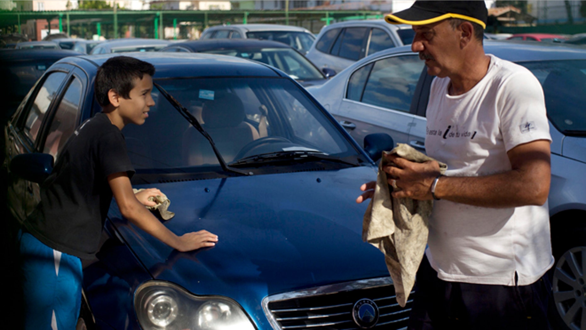 A car dealership worker, right, and a boy clean a used Chinese Geely for sale at a government-run dealership in Havana, Cuba, Thursday, Jan. 2, 2014. This car once was for sale for $5,000 dollars, but the price has risen to as much as $30,000, after a new law took effect eliminating a special permit requirement that has greatly restricted vehicle ownership in the country. (AP Photo/Ramon Espinosa)