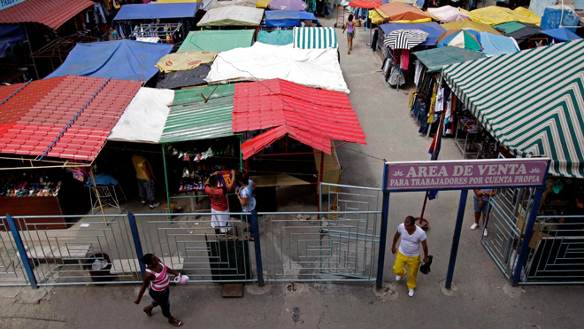 People walk in an open-air market where the government allows licensed vendors to sell their goods in Havana, Cuba, Friday, Aug. 31, 2012. The entrance sign reads in Spanish "Sales area for the self-employed." A jump in import taxes on Monday, Sept. 3 threatens to make life tougher for some of Cuba's new entrepreneurs who the government has been trying to encourage as it cuts a bloated workforce in the socialist economy. In Cuba, the average monthly wage is about $20. (AP Photo/Franklin Reyes)