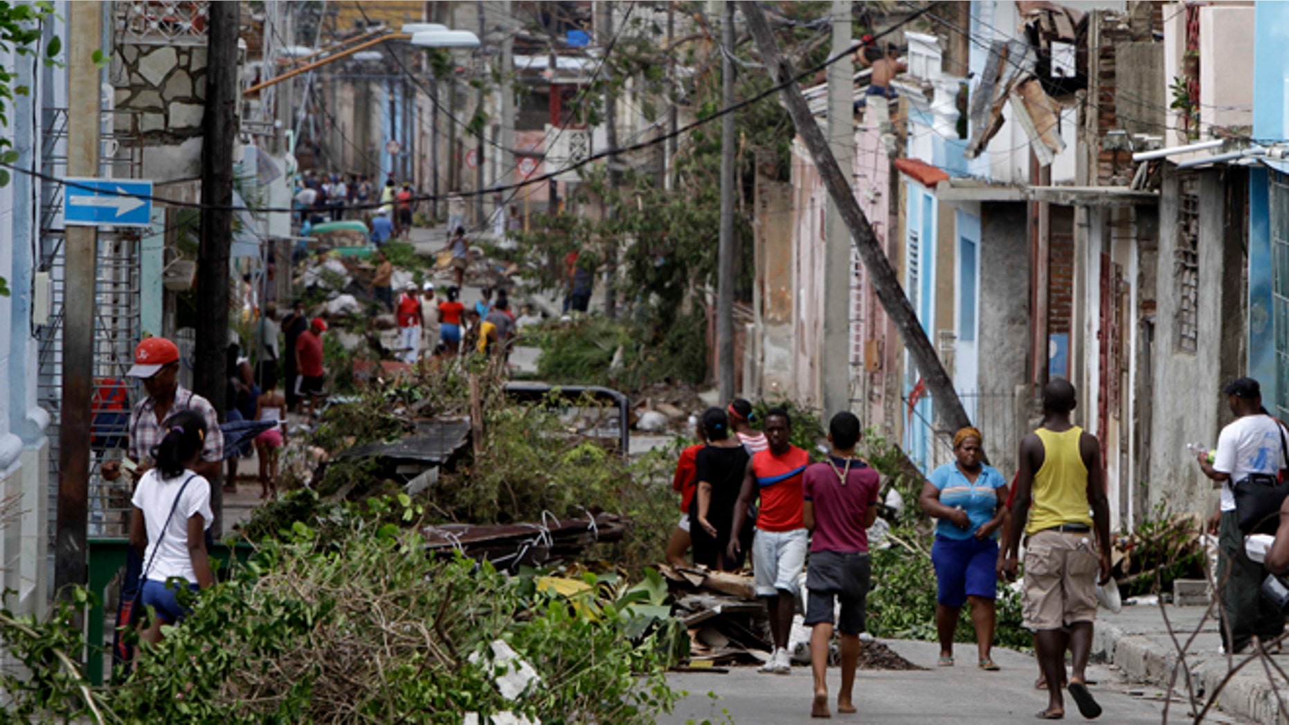 In this Oct. 26, 2012 photo, residents walk past tree branches and power lines felled by Hurricane Sandy in Santiago de Cuba. Residents of Cuba's second city continued to find themselves without power or running water, Monday, Oct. 29, 2012, four days after Hurricane Sandy hit. (AP Photo/Franklin Reyes)