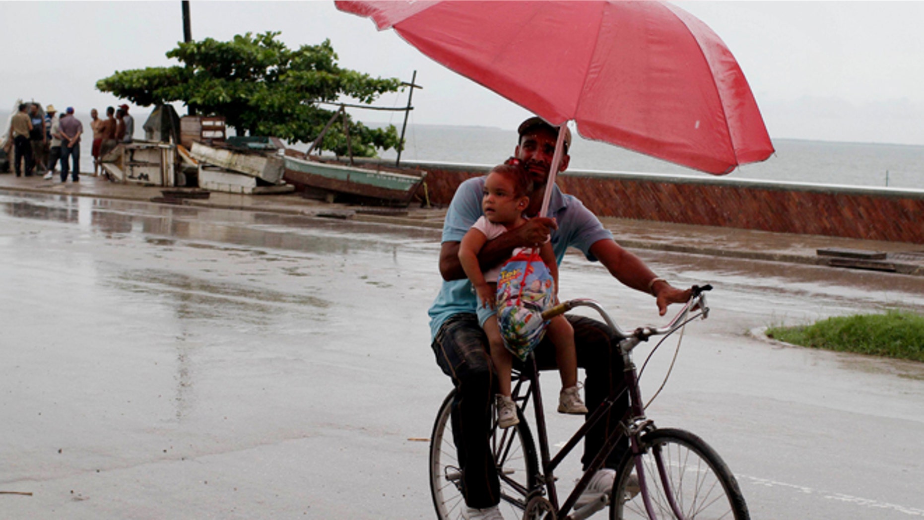 A man balances a child and umbrella on his bike as it rains during the approach of Hurricane Sandy in Manzanillo, Cuba, Wednesday, Oct. 24, 2012. Hurricane Sandy pounded Jamaica with heavy rain as it headed for landfall near the country's most populous city on a track that would carry it across the Caribbean island to Cuba, and a possible threat to Florida. (AP Photo/Franklin Reyes)