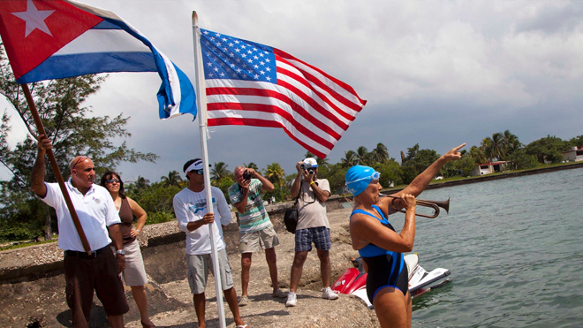 U.S. swimmer Diana Nyad plays a trumpet and points to Florida before starting her swim as people from the local nautical club hold a Cuban and U.S. flag behind her in Havana, Cuba, Saturday, Aug. 18, 2012. Endurance athlete Nyad launched another bid Saturday to set an open-water record by swimming from Havana to the Florida Keys without a protective shark cage. (AP Photo/Ramon Espinosa)