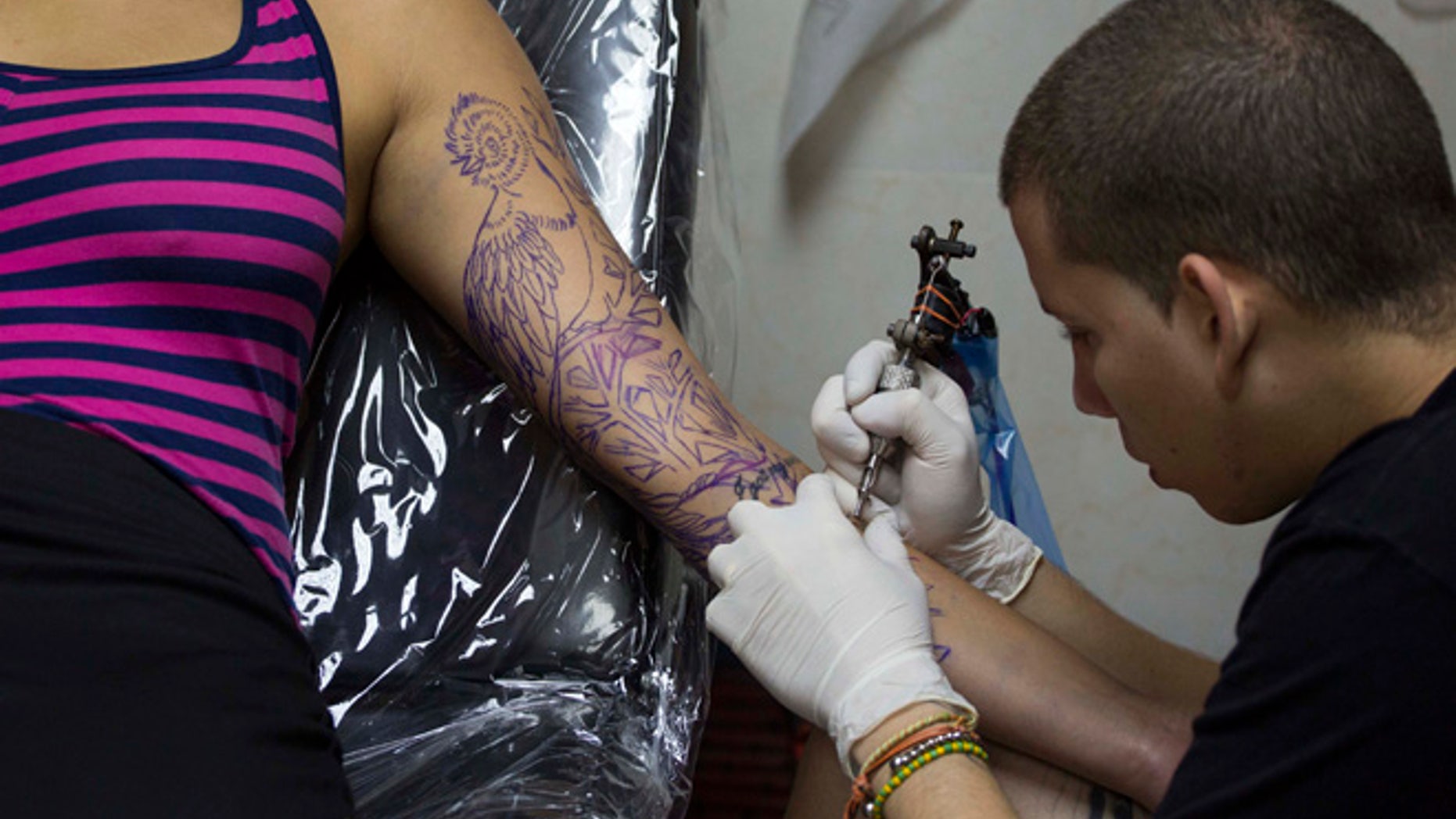 In this Feb. 5, 2016 photo, tattoo artist Mauro Coca works on a tropical bird down the length of arm of Julivic Marquez's arm in Havana, Cuba. The studio where Coca works, La Marca, or The Brand, is an example of Cuba's new acceptance of tattooing. The shop opened a year ago on one of Old Havana's busiest streets and has inked hundreds of tattoos for a mix of Cuban and foreign clients. It's been used as a space for government-sponsored art events and its managers say they've never had any trouble with the state despite their lack of a license explicitly permitting tattooing. (AP Photo/Desmond Boylan)