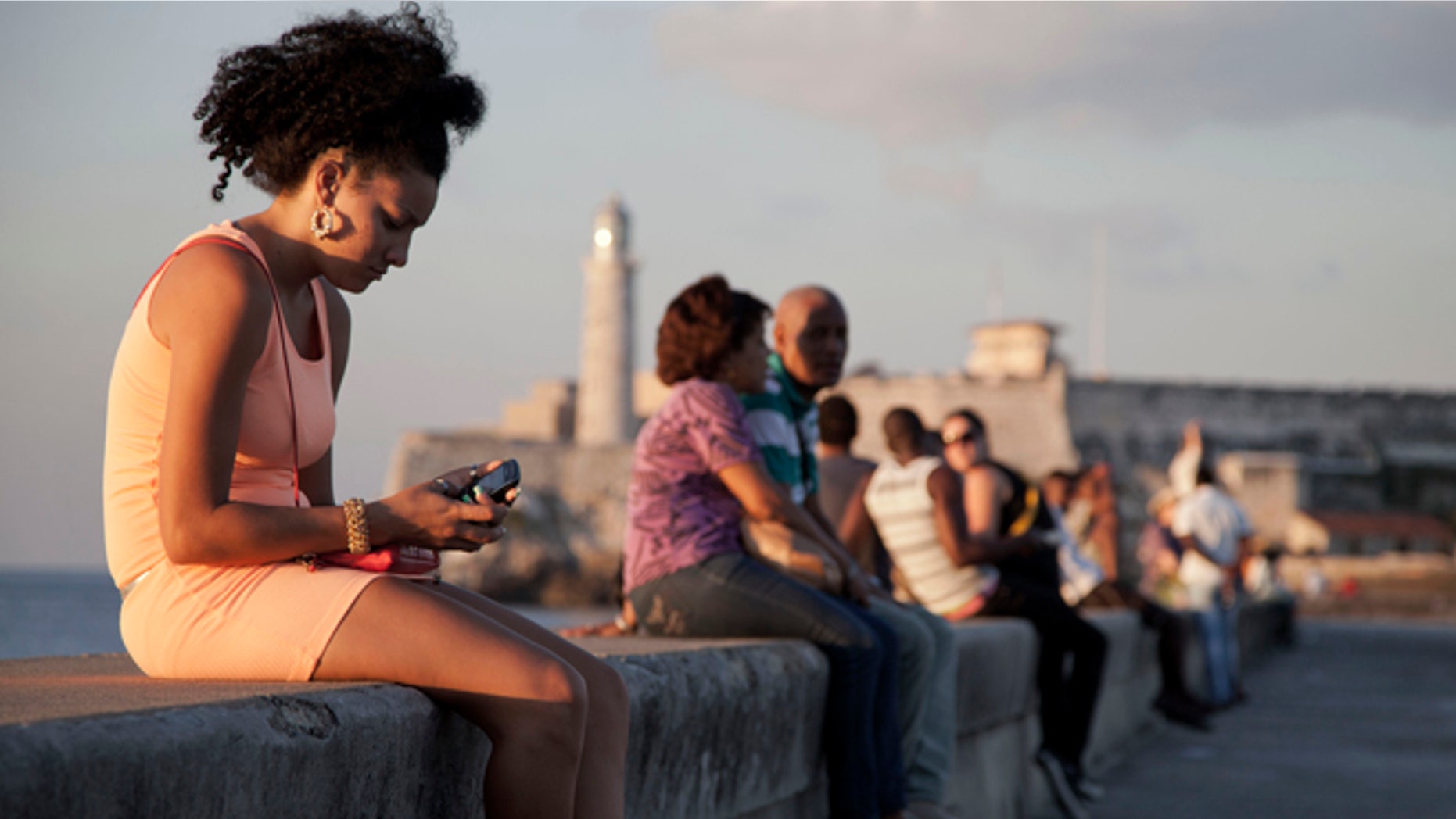 In this March 11, 2014 photo, a woman uses her cellphone as she sits on the Malecon in Havana, Cuba. The U.S. Agency for International Development masterminded the creation of a "Cuban Twitter," a communications network designed to undermine the communist government in Cuba, built with secret shell companies and financed through foreign banks, The Associated Press has learned. The project, which lasted more than two years and drew tens of thousands of subscribers, sought to evade Cubas stranglehold on the Internet with a primitive social media platform. (AP Photo/Franklin Reyes)