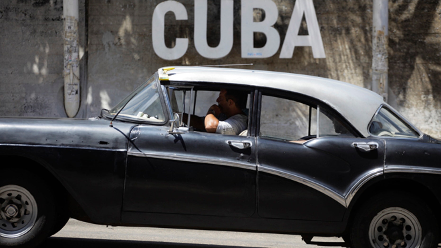A man drives his taxi past a Cultural Center with the word "Cuba" on it, in Havana, Cuba.