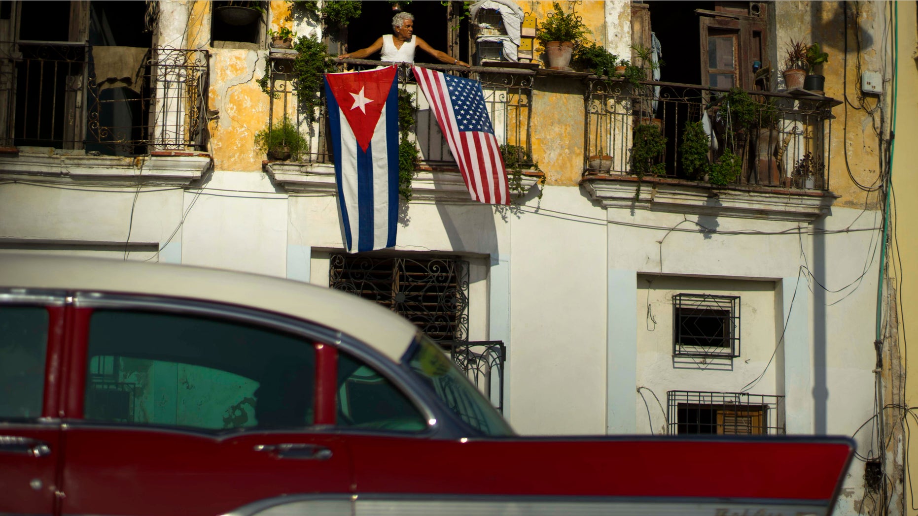 En esta imagen de archivo, tomada el 20 de julio de 2015, Javier Yáñez mira desde un balcón donde están colgadas banderas de Estados Unidos y Cuba, para celebrar las recuperadas relaciones diplomáticas entre Cuba y Estados Unidos, en la Vieja Habana. El gobierno cubano no ha anunciado todavÃa ningún gran acuerdo con empresas estadoundienses desde el histórico anuncio del pasado 17 de diciembre. (Foto AP/Ramon Espinosa, archivo)
