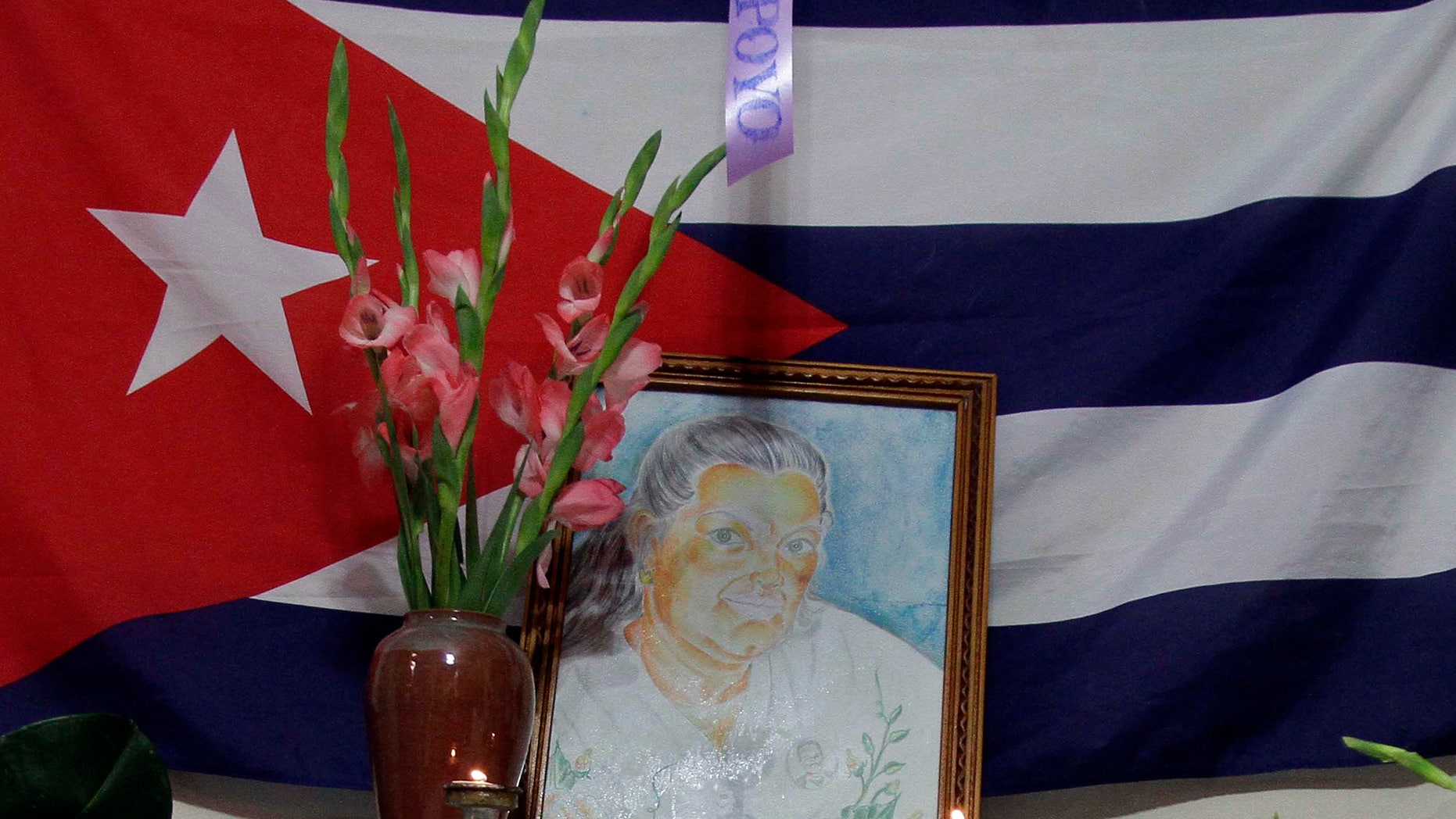 A painting of Laura Pollan, late leader of the dissident group "Ladies in White," is flanked by flowers, candles and a Cuban flag during a gathering in her honor at her home in Havana, Cuba, Saturday Oct. 15, 2011. According to Elizardo Sanchez, head of the Cuban Commission for Human Rights and National Reconciliation, Pollan died of a cardio-respiratory attack on Friday Oct. 14, 2011. (AP Photo/Franklin Reyes)