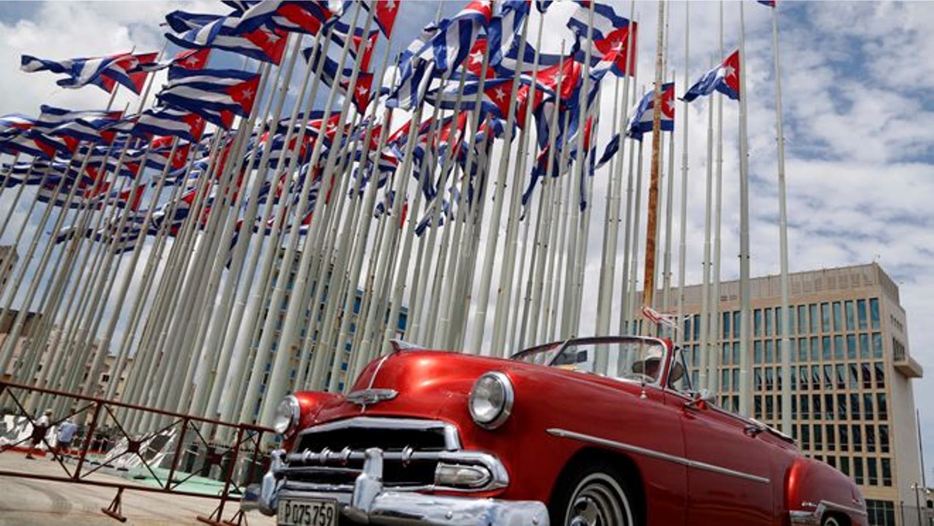 FILE - In this July 26, 2015, file photo, a classic American convertible car passes beside the United States embassy as Cuban flags fly beside in Havana, Cuba. The U.S. doesnt plan to invite Cuban dissidents to Secretary of State John Kerrys historic flag-raising at the American Embassy in Havana on Aug. 14, illustrating a shift in U.S. policy from the islands opposition to its government. (AP Photo/Desmond Boylan, File)