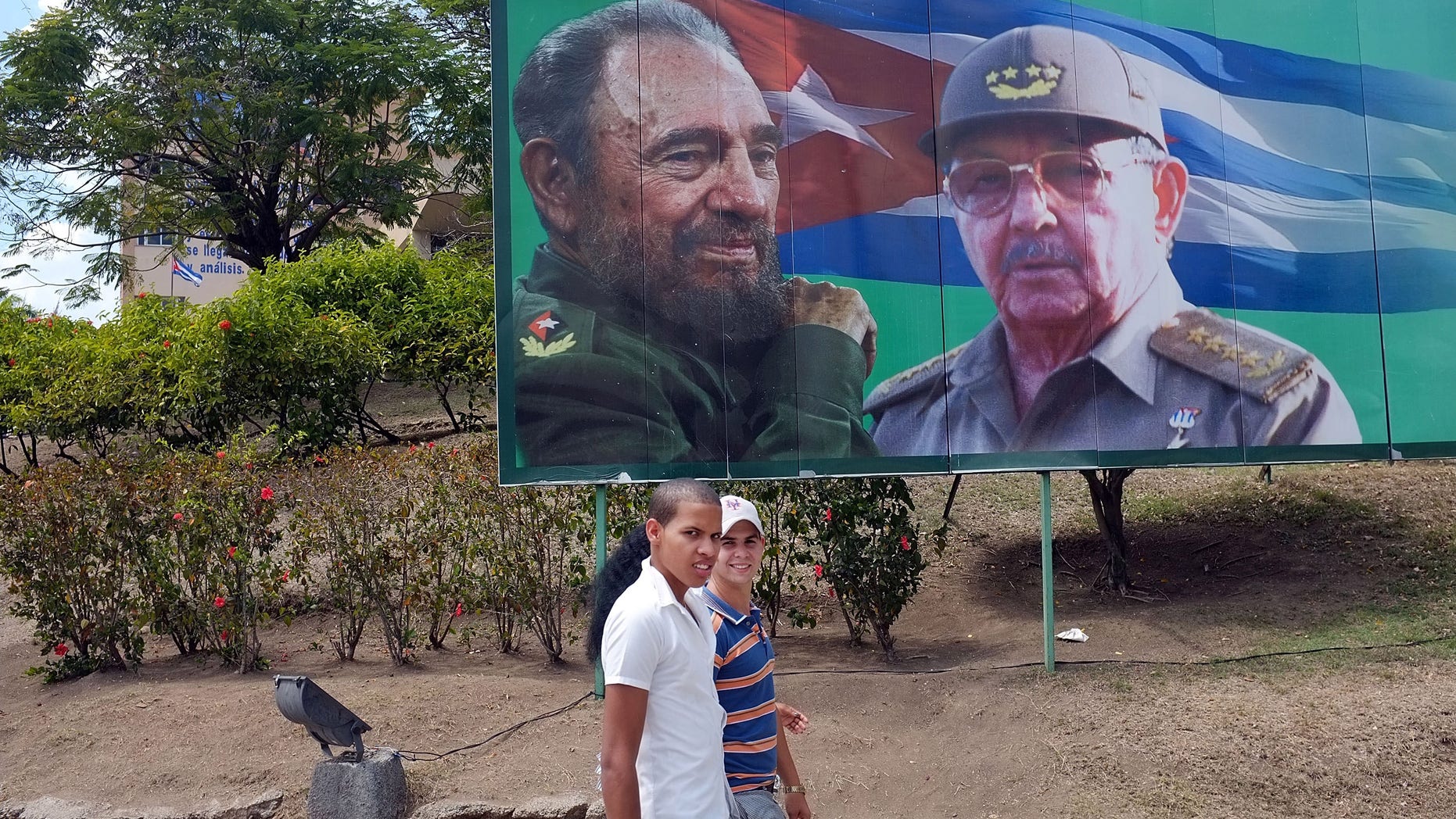 SANTIAGO DE CUBA, CUBA - MARCH 27: Two teens walk by a billboard of Fidel and Raul Castro a day after Pope Benedict XVI held a historic mass in the city on March 27, 2012 in Santiago de Cuba. Fourteen years after Pope John Paul II visited Cuba, Pope Benedict is making his first trip to the communist country. Benedict, who arrived from Mexico, conducted a mass in the city of Santiago de Cuba first followed by a mass in Havana before leaving on the 28th. Tensions are high in Cuba between dissidents and the government as activists hope the international exposure of the Papal visit will result in renewed attention to their struggle for greater freedoms. (Photo by Spencer Platt/Getty Images)