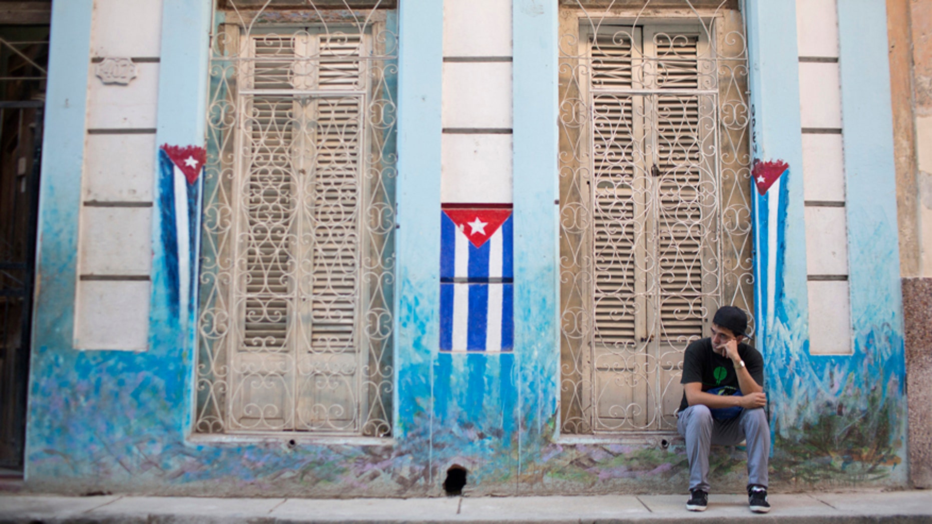 File photo - A man sits on the sidewalk next to Cuban National flags painted on the walls in downtown Havana, Jan. 22, 2015.
