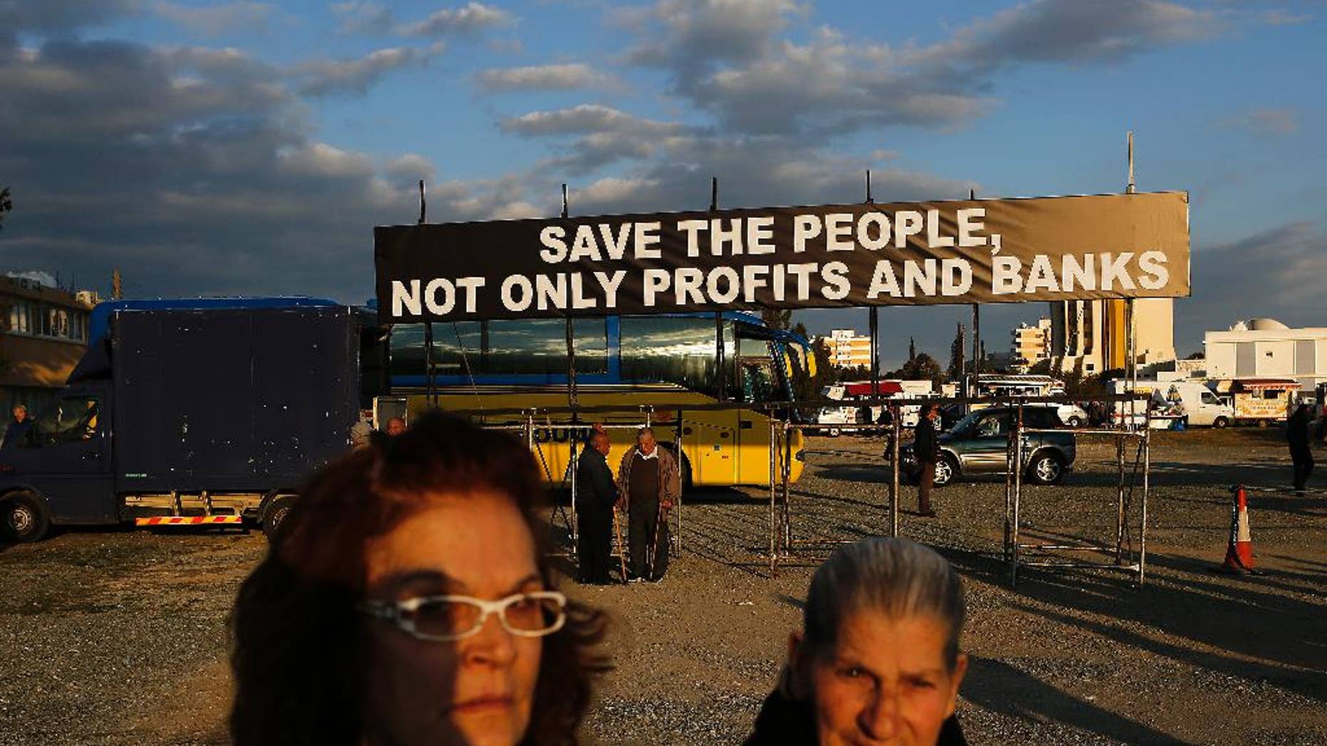 Two protestors walk in front of a banner during an anti austerity demonstration outside a European Central Bank Governing Council meeting at the conference center in capital Nicosia, Cyprus, Wednesday, March 4, 2015. Several thousand demonstrators in Cyprus called for an end to austerity policies they say has driven many in the bailed-out country to poverty. (AP Photo/Petros Karadjias)