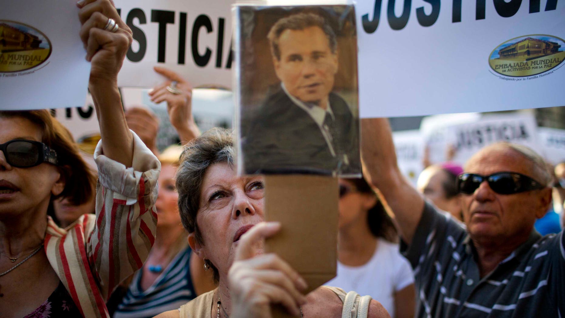 A woman chants the Argentine national anthem holding a portrait of the late prosecutor Alberto Nisman outside the AMIA Jewish community center in Buenos Aires, Argentina, Wednesday, Jan. 21, 2015. Nisman, who had been investigating the 1994 bombing of the Jewish community center that killed 85 people and who accused President Cristina Fernandez of shielding Iranian suspects, was found dead from a gunshot to the head, in his apartment late Sunday, hours before he was to testify in a Congressional hearing about the case. (AP Photo/Rodrigo Abd)