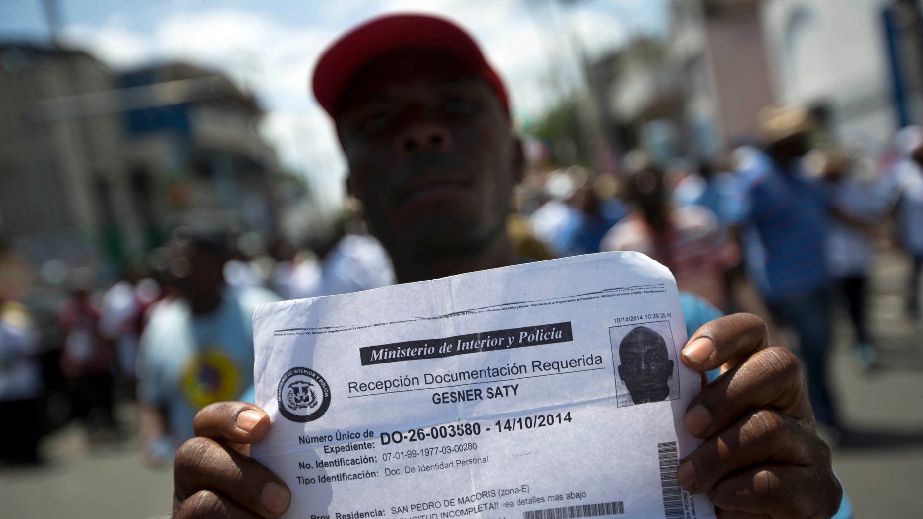 FILE - In this July 21, 2015, file photo, deported Haitian man holds up his document that confirms he turned in paperwork to apply for legal residency in the Dominican Republic during a march to the prime minister's office to protest the DR's deportation of Haitians in Port-au-Prince, Haiti. The sharply uneven situation for non-citizens stems from a 2013 ruling by the Dominican Constitutional Court in a decades-long dispute over who is entitled to citizenship. (AP Photo/Dieu Nalio Chery, File)
