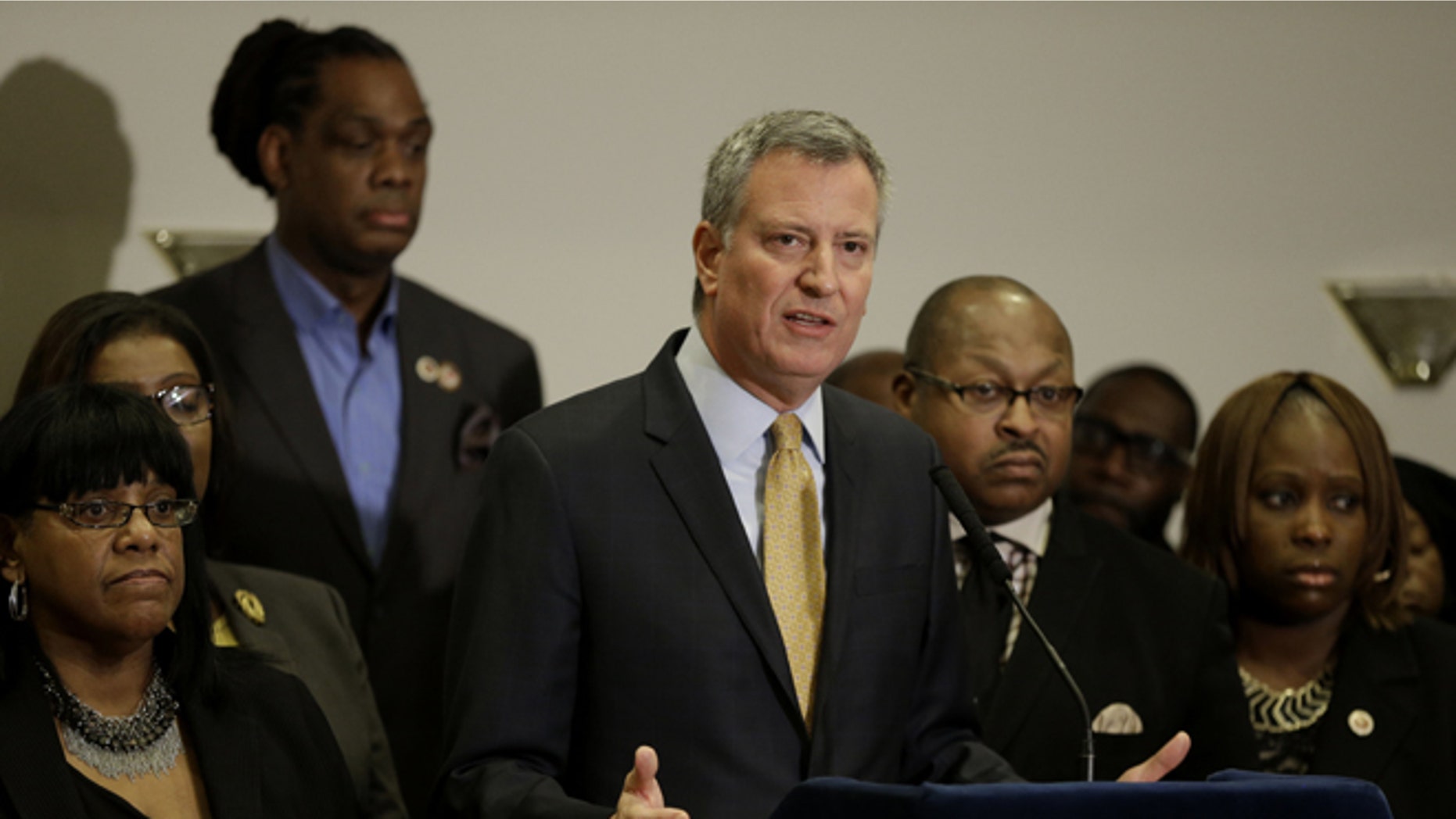 New York City Mayor Bill de Blasio, surrounded by community leaders, speaks to reporters about the grand jury's decision in the Eric Garner case in the borough of Staten Island in New York, Wednesday, Dec. 3, 2014. A grand jury cleared the white New York City police officer Wednesday in the videotaped chokehold death of Garner, an unarmed black man, who had been stopped on suspicion of selling loose, untaxed cigarettes, a lawyer for the victim's family said. A video shot by an onlooker and widely viewed on the Internet showed the 43-year-old Garner telling a group of police officers to leave him alone as they tried to arrest him. The city medical examiner ruled Garner's death a homicide and found that a chokehold contributed to it. (AP Photo/Seth Wenig)