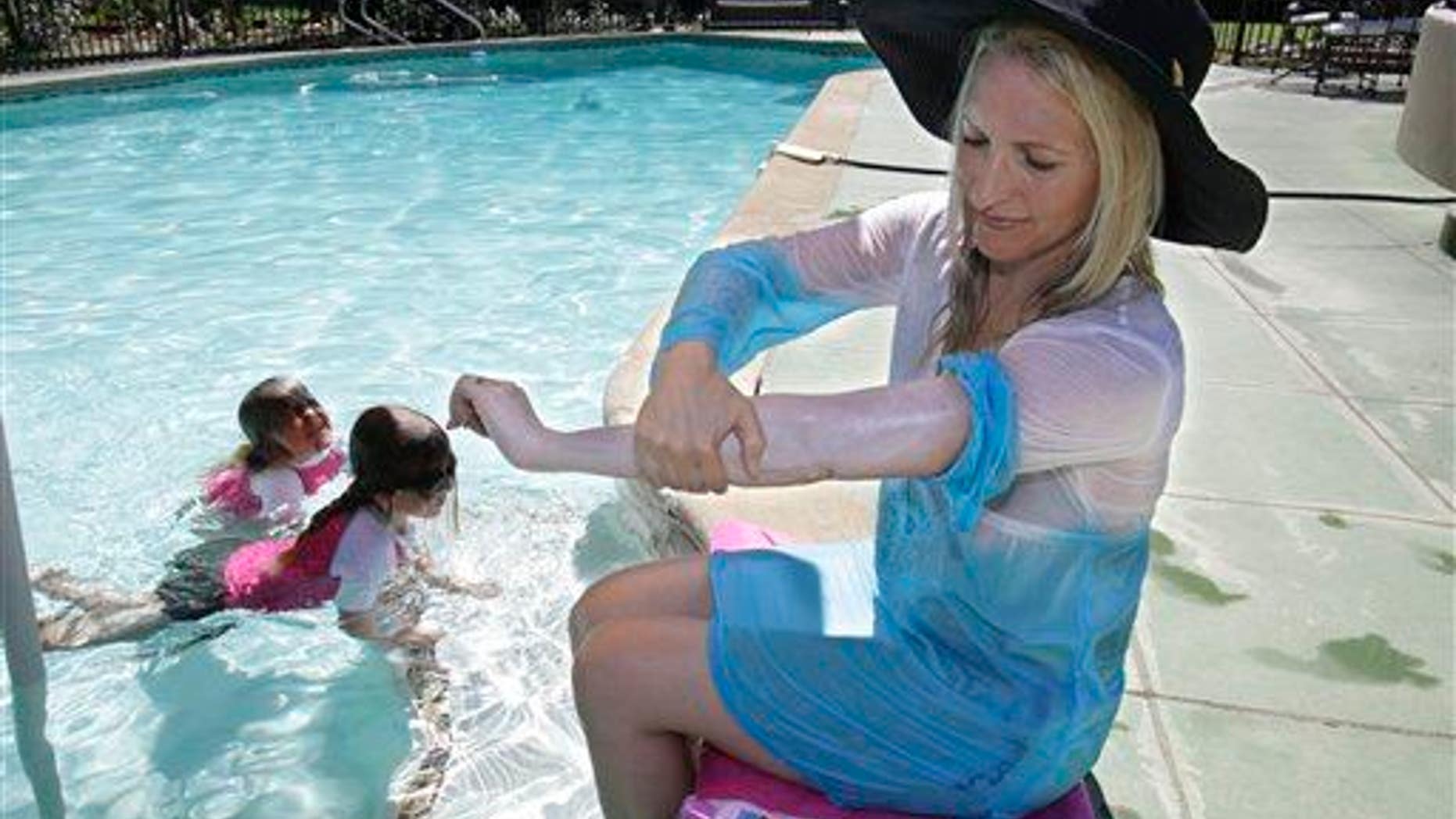 In this Wednesday, June, 22, 2011, photo, a woman who was diagnosed with malignant melanoma at 35 puts on sun screen while poolside with her daughters at their home in Carmichael, Calif.