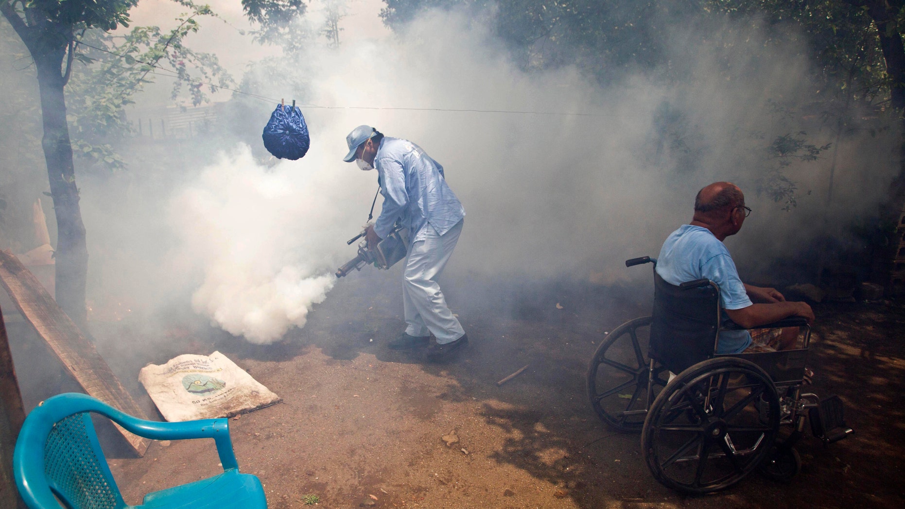 A worker from the health ministry fumigates the backyard of a home where the man who lives there sits in his wheelchair in the neighborhood of Waspam in Managua, Nicaragua.