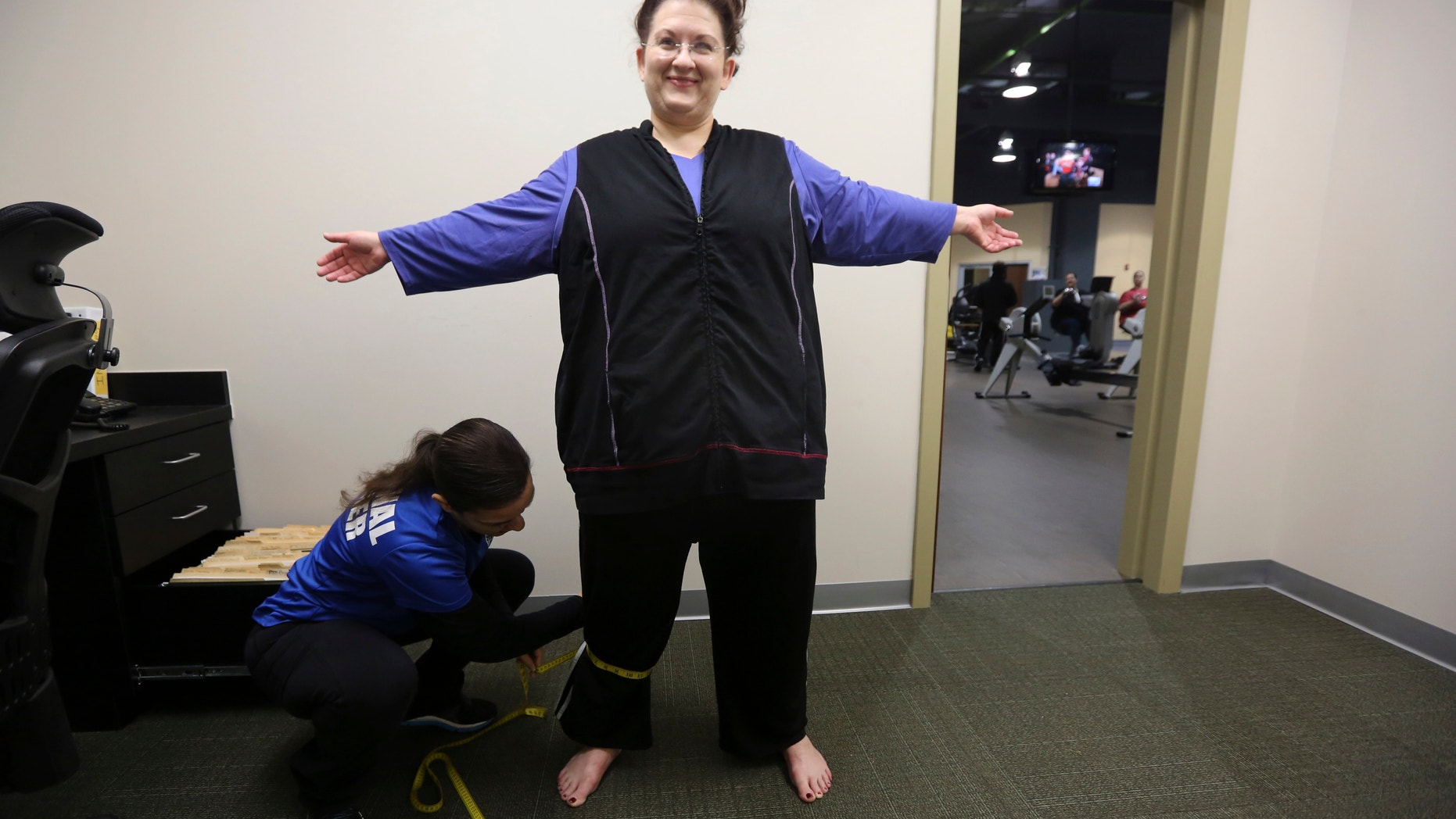 Personal trainer Krisaane Hale, bottom, measures Ellen Hays for body mass index reading before working out in a morning exercise class at the Downsize Fitness gym in Addison, Texas.