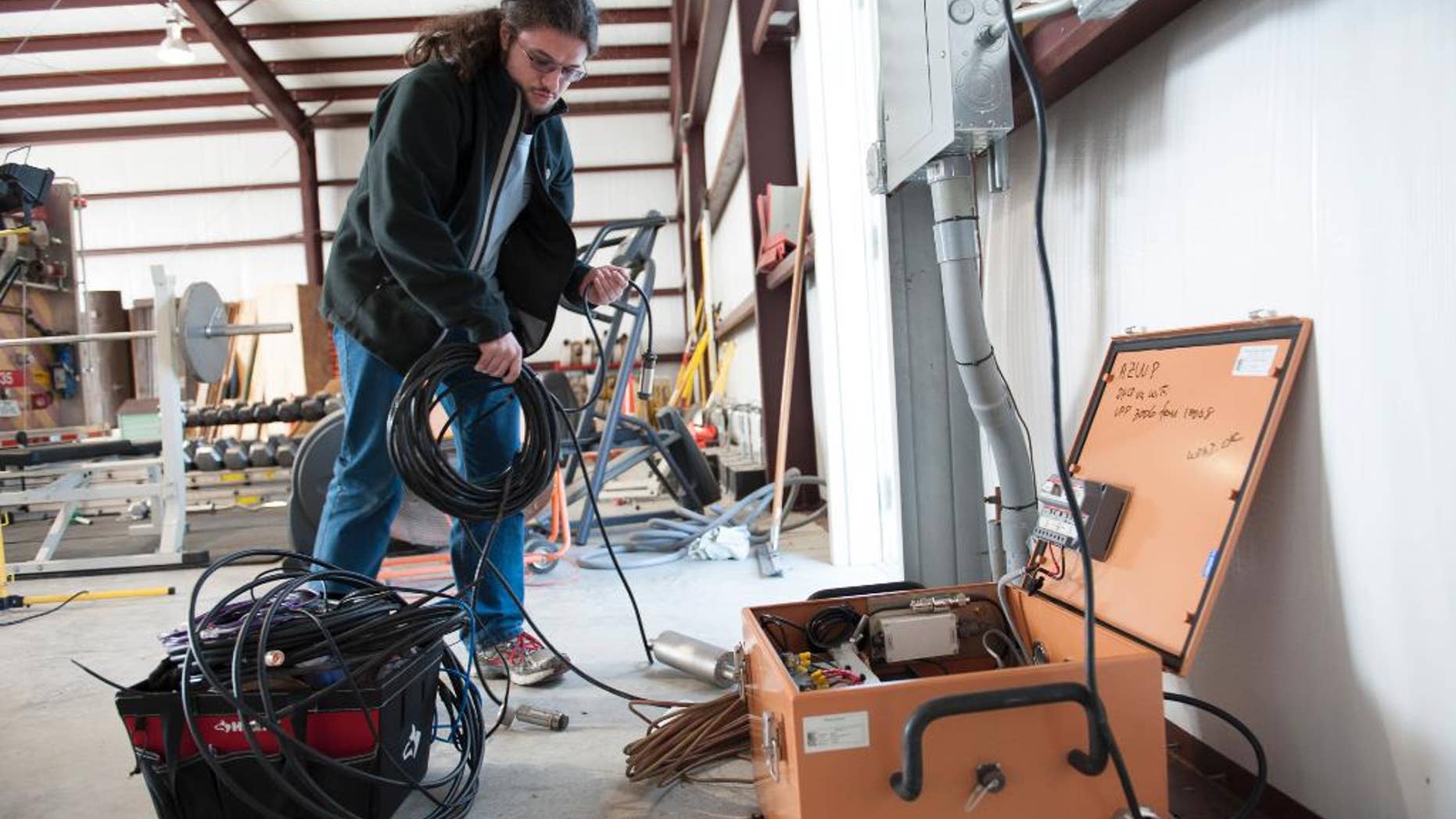This handout photo, taken Jan. 16, 2014, provided by Southern Methodist University, shows Remi Oldham, an SMU geophysics graduate student, running a cable to connect the seismometer to communications interface equipment housed in the orange metal box in Willow Park, Texas. The interface equipment allows the transmission of the data collected by the seismometer back to SMU. With real-time monitors, scientists linked a swarm of small earthquakes west of Fort Worth, Texas, to nearby natural gas wells and wastewater injection. In 84 days from November 2013 to January 2014, the area around Azle, Texas, shook with 27 magnitude 2 or greater earthquakes, while scientists at Southern Methodist University and the U.S. Geological Survey monitored the shaking. It’s an area that had no recorded quakes for 150 years on faults that “have been inactive for hundreds of millions of years,” said SMU geophysicist Matthew Hornbach. (Hillsman Stuart Jackson/SMU via AP) SMU, Dedman School of Humanities, Geology, Research, Seismic, Off Campus, Willow Park, Texas, Secondary Fire Station, Heather Deshon, Chris Hayward, Remi Oldham