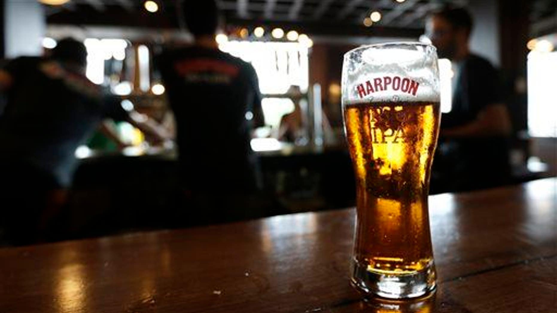In this July 1, 2013 photo a glass of Rich and Dan's Rye IPA rests on the counter as bartenders pour drafts for patrons in the Beer Hall at the Harpoon Brewery in the Seaport District of Boston.