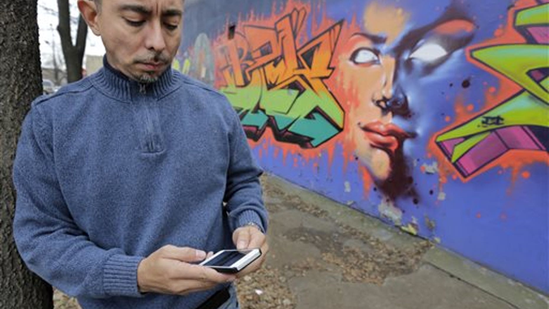 In this Dec. 6, 2013 photo, Eddie Bocanegra, co-executive director of the YMCA of Metropolitan Chicago's Youth Safety and Violence Prevention program, stands with his phone outside the organization's center in the Pilson neighborhood of Chicago. With the advent of social media usage by gangs, he says, "In the past you would have gangs approach you and say, 'Listen we're from the 'hood. Maybe you should get involved.' Now the kids are going to the gangs saying, 'I saw this. How can I be a part of it?'" (AP Photo/M. Spencer Green)
