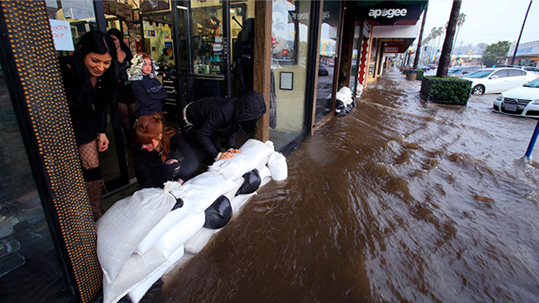 From left, Amanda Bourbois, Mary Spear and Jordan Brown place sand bags in front of the Electric Chair salon Wednesday, Jan. 6, 2016, in San Diego. El Nino storms lined up in the Pacific, promising to drench parts of the West for more than two weeks and increasing fears of mudslides and flash floods in regions stripped bare by wildfires. (Nelvin C. Cepeda/The San Diego Union-Tribune via AP) NO SALES; MANDATORY CREDIT