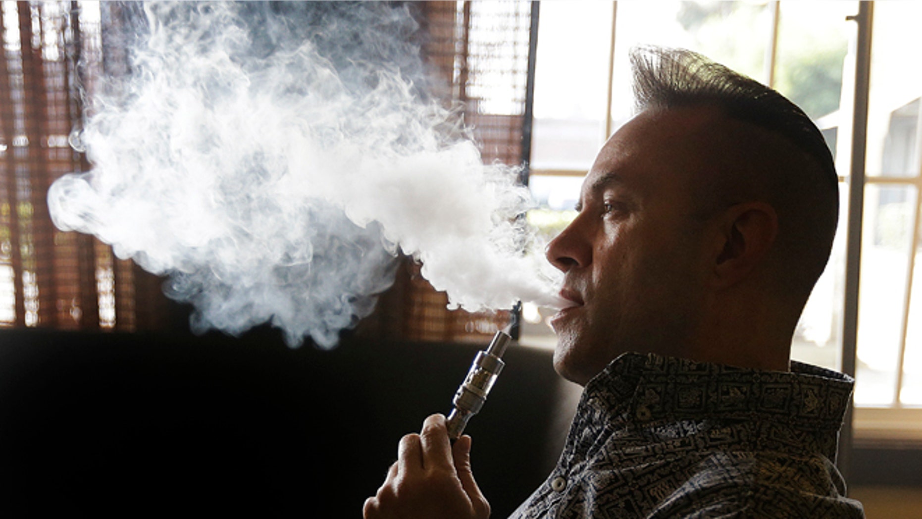 Geoff Braithwaite, owner of Tasty Vapor, exhales vapor after using an electronic cigarette Wednesday, Jan. 28, 2015, in Oakland, Calif. California health officials on Wednesday declared electronic cigarettes a health threat that should be strictly regulated like tobacco products, joining other states and health advocates across the U.S. in seeking tighter controls as "vaping" grows in popularity. The California Department of Public Health report says e-cigarettes emit cancer-causing chemicals and get users hooked on nicotine but acknowledges that more research needs to be done to determine the immediate and long-term health effects. (AP Photo/Ben Margot)