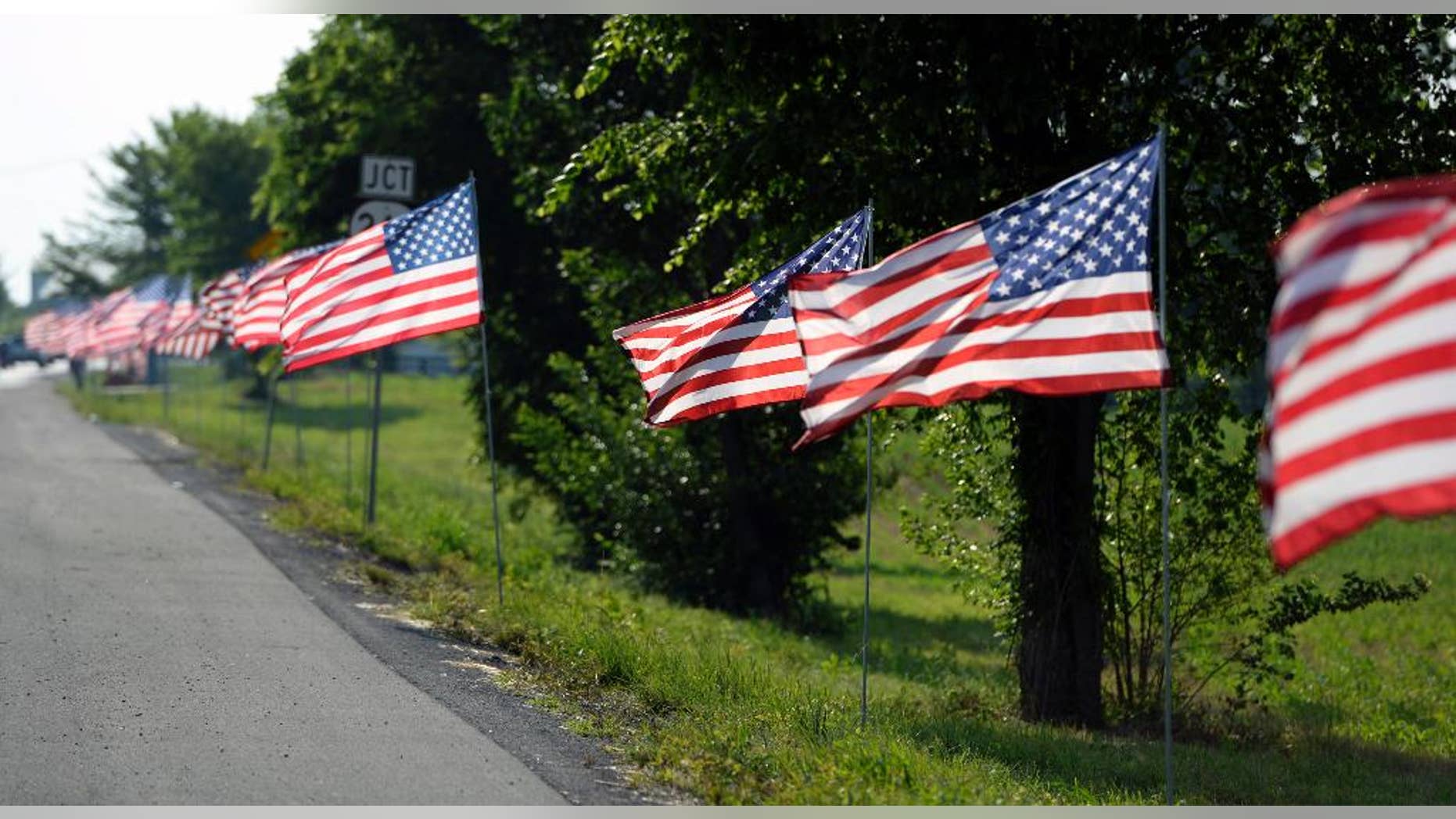 FILE - In this Thursday, May 30, 2013, photo, United States flags line the route of the funeral procession of Bardstown, Ky. Officer Jason Ellis during his funeral service The shocking murder of the ex-minor league baseball player and father of two young boys still haunts Ellis’ colleagues and the town of about 12,000 in Kentucky’s bourbon country. In the ensuing months, tips poured in, police dangled about $200,000 in reward money and billboards publicized the case. (AP Photo/Timothy D. Easley, File)