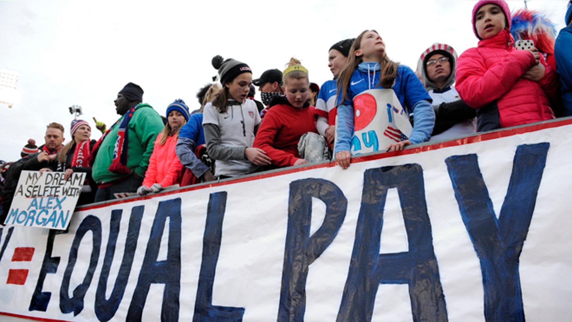Fans stand behind a large sign for equal pay for the women's soccer team during an international friendly soccer match between the United States and Colombia at Pratt & Whitney Stadium at Rentschler Field, Wednesday, April 6, 2016, in East Hartford, Conn. (AP Photo/Jessica Hill)