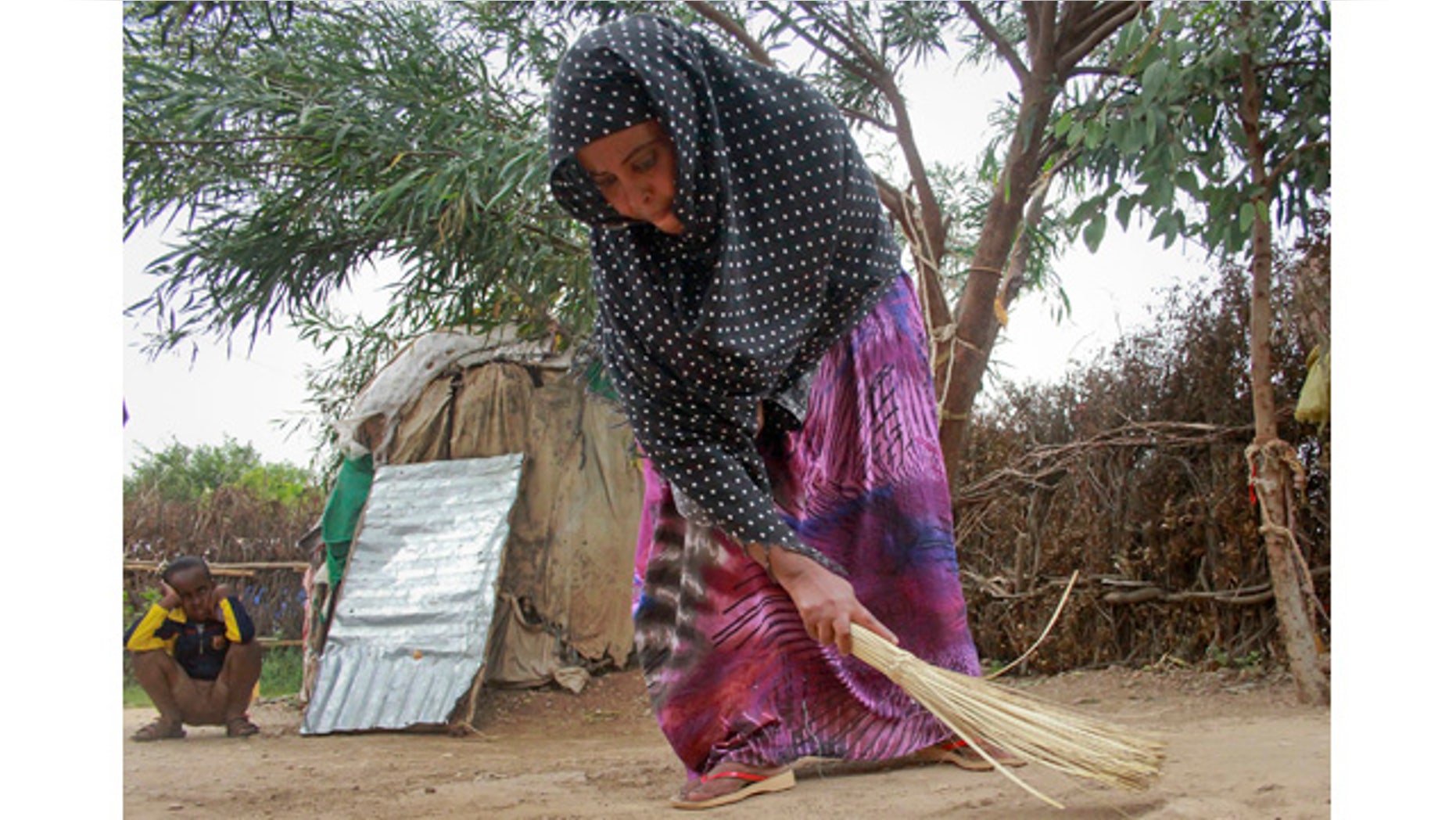 April 27, 2014: Ubah Mohammed Abdule, 33, center, sweeps the floor outside her hut as her son Abdullahi Yusuf Ahmed, 8, left, looks on in the Shedder refugee camp near the town of Jigjiga, in far eastern Ethiopia. (AP Photo/Elias Asmare)
