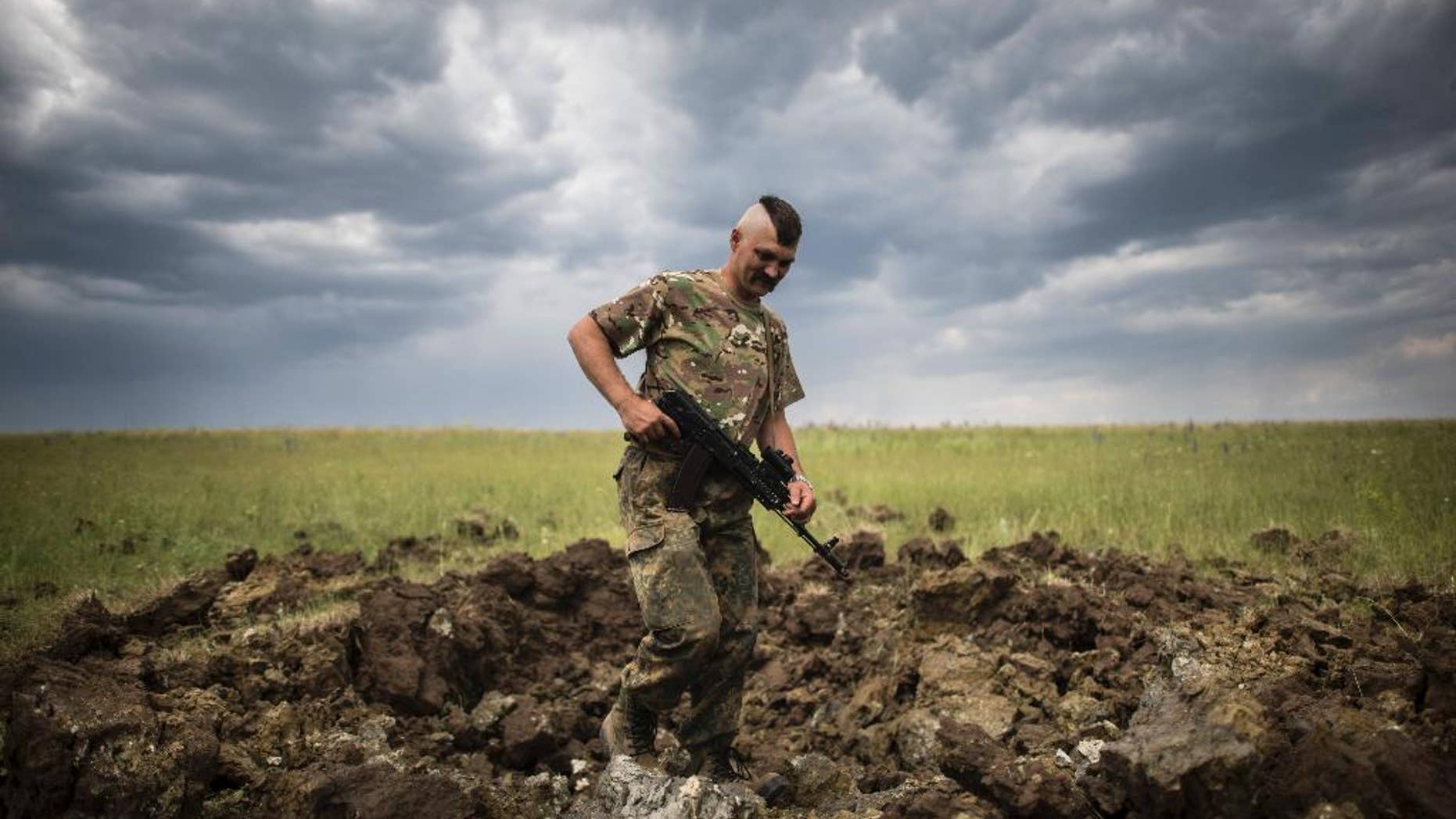 FILE - In this Monday, June 15, 2015 file photo, a Ukrainian serviceman investigates a crater left by a Grad rocket in the village of Toshkivka, Luhansk region, eastern Ukraine. (AP Photo/Evgeniy Maloletka, File)