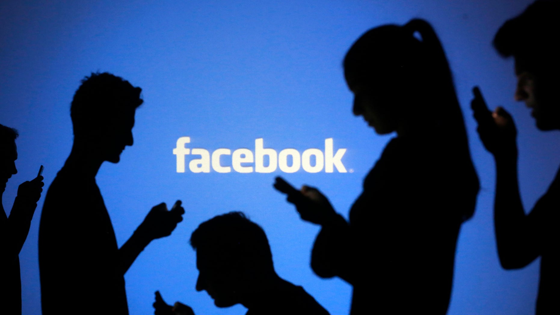 People are silhouetted as they pose with mobile devices in front of a screen projected with a Facebook logo, in this picture illustration taken in Zenica October 29, 2014. Facebook Inc warned on Tuesday of a dramatic increase in spending in 2015 and projected a slowdown in revenue growth this quarter, slicing a tenth off its market value. Facebook shares fell 7.7 percent in premarket trading the day after the social network announced an increase in spending in 2015 and projected a slowdown in revenue growth this quarter. REUTERS/Dado Ruvic (BOSNIA AND HERZEGOVINA - Tags: BUSINESS SCIENCE TECHNOLOGY BUSINESS LOGO) - RTR4C0UZ