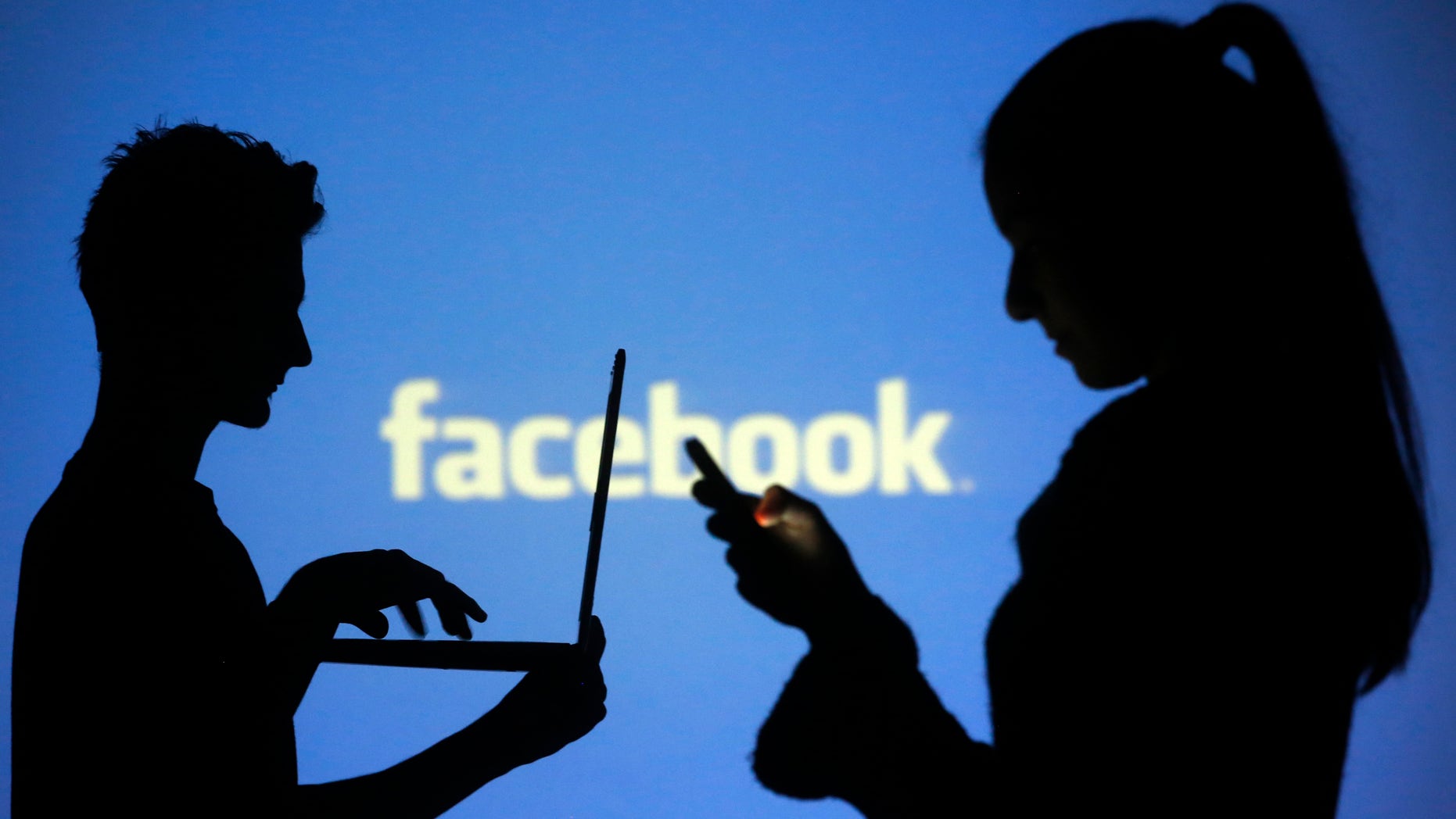 People are silhouetted as they pose with laptops in front of a screen projected with a Facebook logo, in this picture illustration taken in Zenica October 29, 2014. Facebook Inc warned on Tuesday of a dramatic increase in spending in 2015 and projected a slowdown in revenue growth this quarter, slicing a tenth off its market value. Facebook shares fell 7.7 percent in premarket trading the day after the social network announced an increase in spending in 2015 and projected a slowdown in revenue growth this quarter. REUTERS/Dado Ruvic (BOSNIA AND HERZEGOVINA - Tags: BUSINESS SCIENCE TECHNOLOGY BUSINESS LOGO) - RTR4C0V2