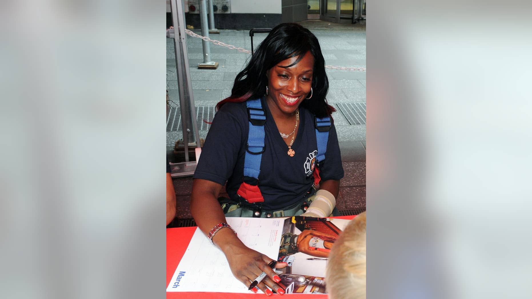 In a photo provided by the New York City Fire Department, firefighter Danae Mines autographs a copy of the 2015 Calendar of Heroes, which features her as Miss March, Tuesday, July 15, 2014, in New York's Times Square. Mines, of Engine Co. 6 in the South Bronx, is an 11-year veteran, one of only 41 female firefighters in the department, and the first female firefighter to appear in the famed charity calendar of hard bodies. (AP Photo/FDNY)