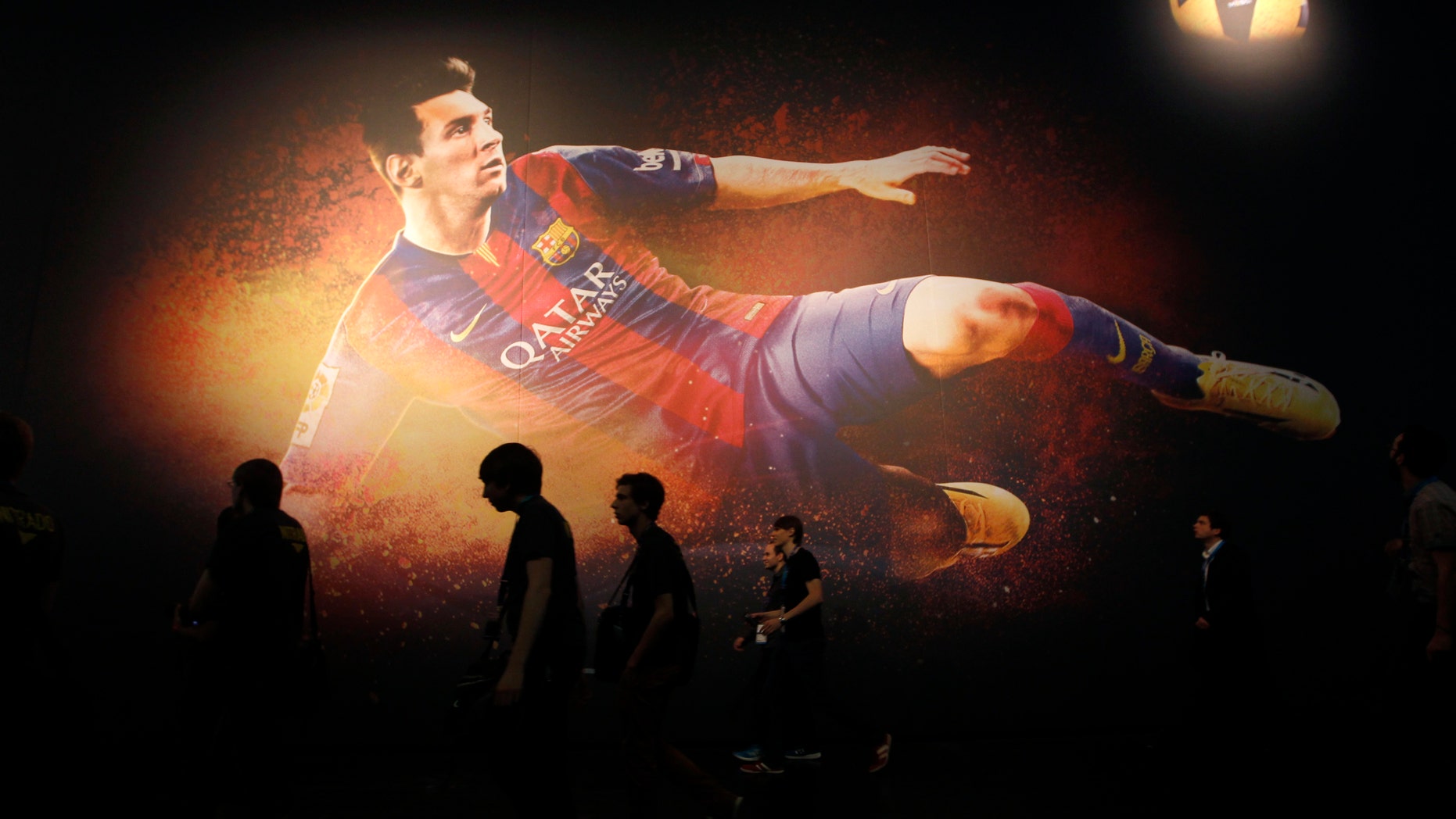 Visitors walk past a placard of "FIFA 15" video game featuring soccer player Lionel Messi at the Gamescom 2014 fair in Cologne Aug. 13, 2014.