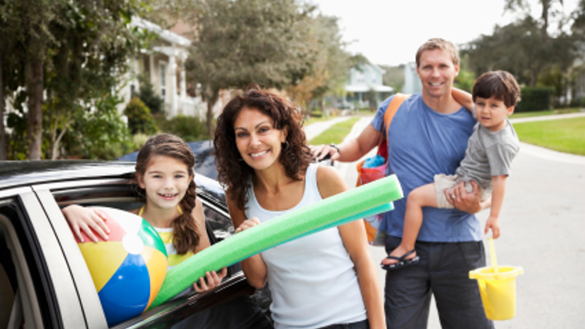 Family with two children (3 and 9 years) packing car for trip to the beach. Focus on mother and daughter.