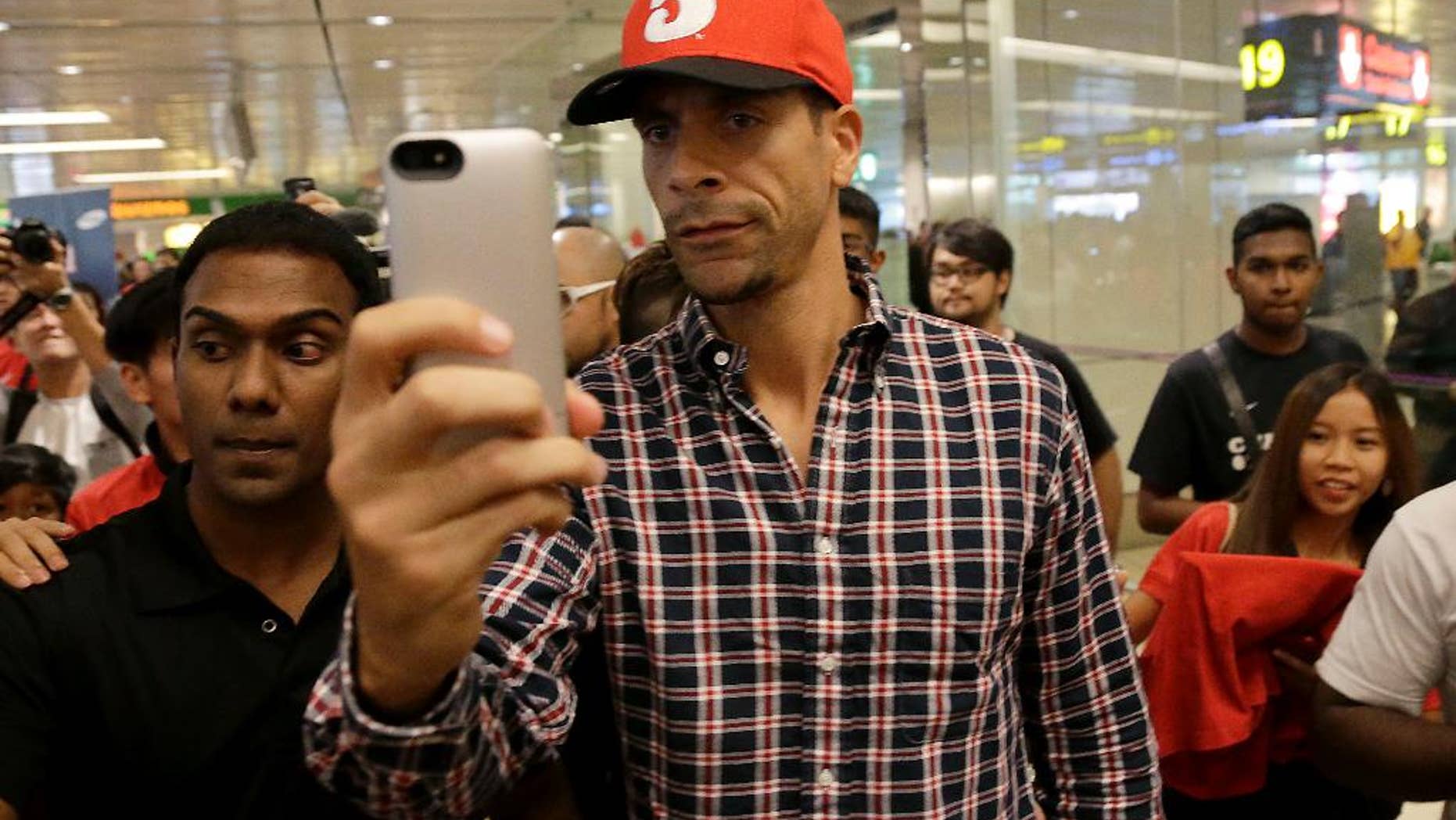 FILE - In this Tuesday, May 13, 2014, Manchester United's Rio Ferdinand takes a "selfie" upon arrival at the Changi International Airport in Singapore. The English Football Association has banned Queens Park Rangers defender Rio Ferdinand for three games over a tweet containing a derogatory reference to women. (AP Photo/Wong Maye-E, File)