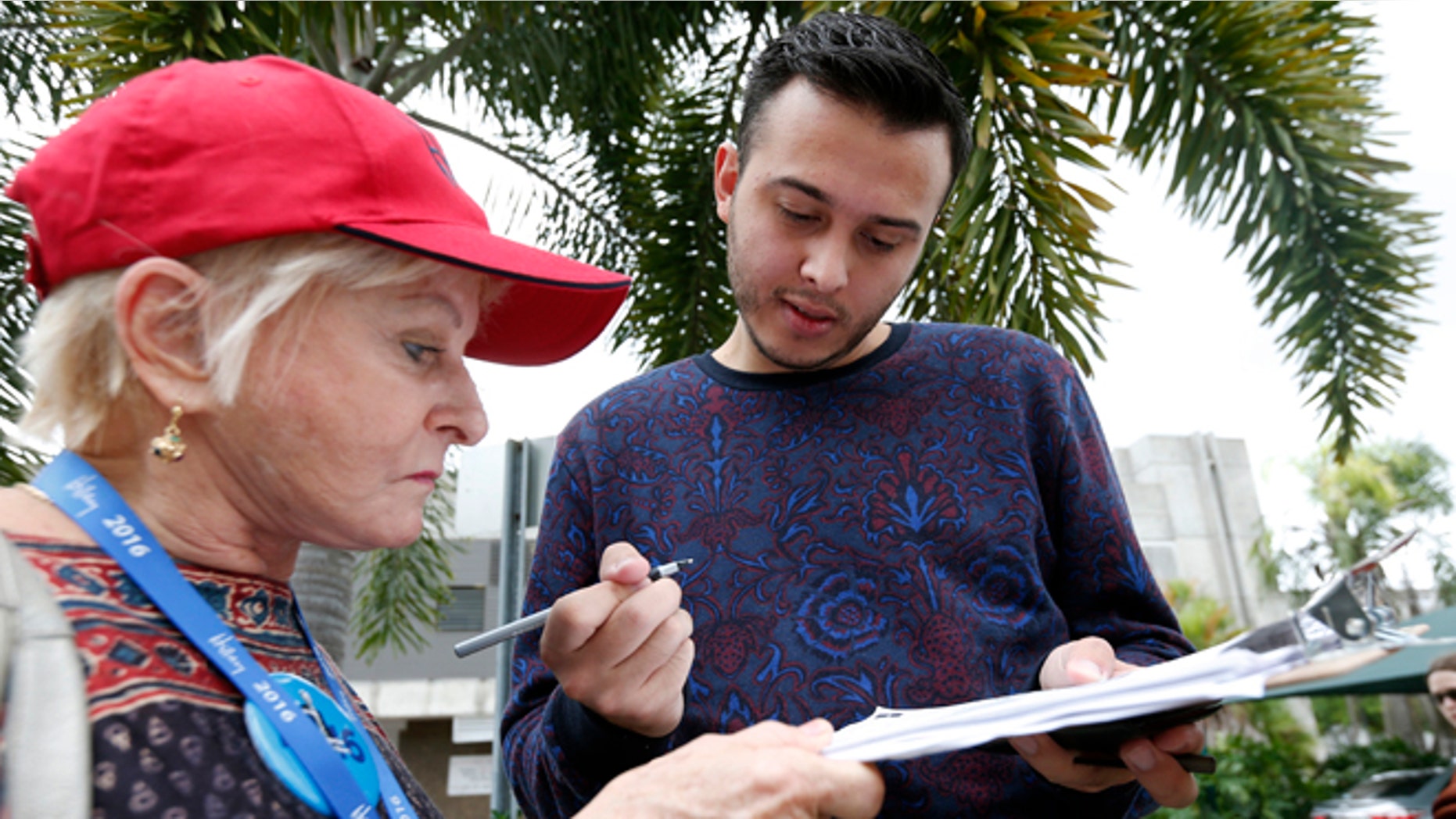 Volunteer Sandi Strickland, left, helps Roman Rodriguez, right, fill out a new voter registration form because of a change of address, as he waits in line to attend a rally for Democratic presidential candidate Hillary Clinton and former vice president Al Gore, Tuesday, Oct. 11, 2016, in Miami. A federal judge has given Democrats a partial victory in the presidential battleground of Florida, extending the state's voter registration deadline one day and agreeing to consider a longer extension in the wake of Hurricane Matthew. (AP Photo/Wilfredo Lee)
