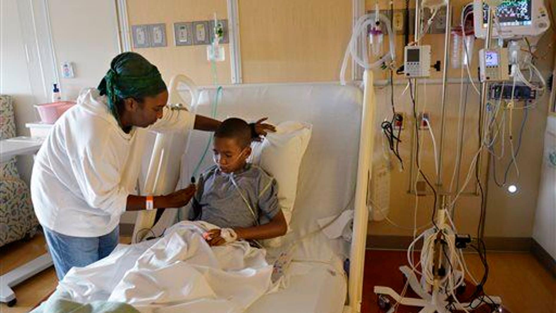 In this Sept. 8, 2014, photo, Melissa Lewis of Denver helps her son, Jayden Broadway, 9, as he coughs in his bed at the Children's Hospital Colorado in Aurora, Colo. He was treated for enterovirus-68.
