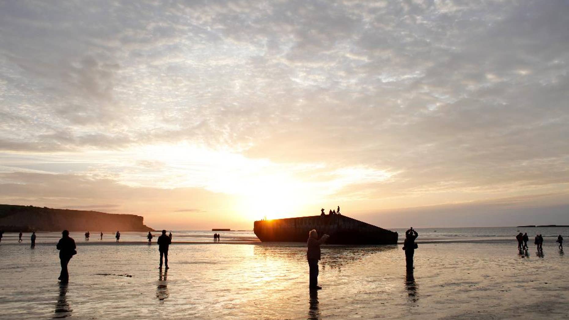 People walk on the beach where remnants of the artificial port of Arromanches, still stand in western France, Thursday June 5, 2014. World leaders and veterans prepare to mark the 70th anniversary of the invasion this week in Normandy. (AP Photo/Thibault Camus)