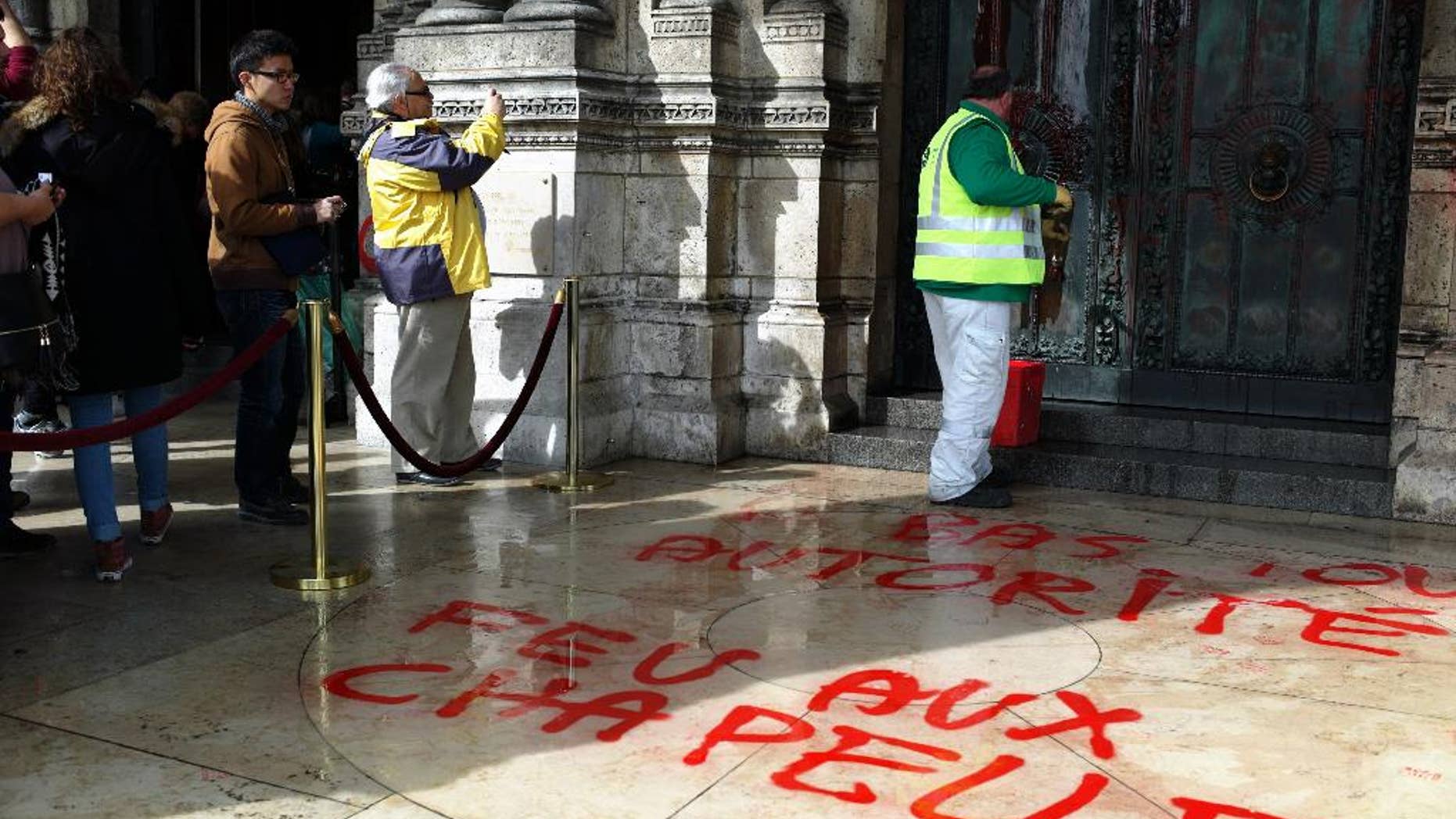 A worker cleans the graffiti at entrance of the Sacre Coeur basilica in the Montmartre district of Paris, Wednesday, March 19, 2014. There were no immediate claims of responsibility for graffiti found at the iconic basilica. Graffiti on the floor reads: Down with any authority. (AP Photo/Thibault Camus)
