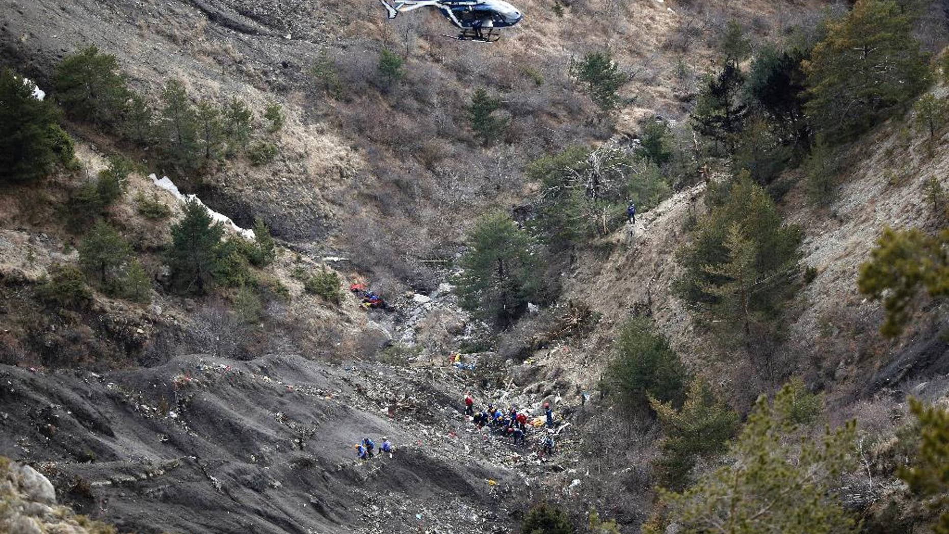 FILE - In this Thursday March 26, 2015 file photo, a helicopter flies over rescue workers at the crash site of the Germanwings jet near Seyne-les-Alpes, France. The somber mission to recover the remains of 150 people killed instantly when the Germanwings flight slammed full speed into the Col de Mariaud is not a quiet one and crucial physical evidence for the crash investigation can be gathered only when the mountains cooperate. (AP Photo/Laurent Cipriani, File)
