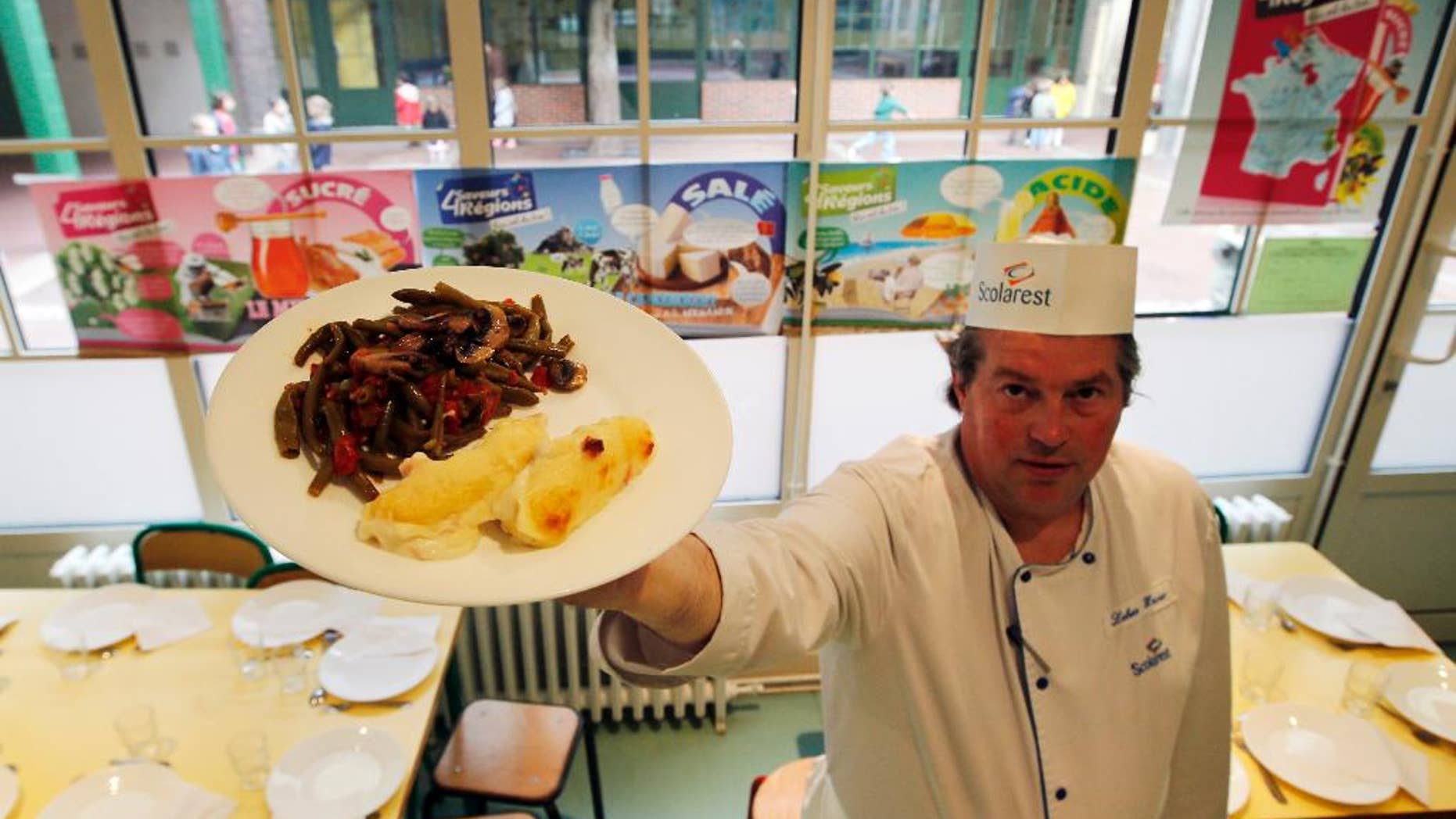 FOR STORY FRANCE SCHOOL LUNCHES - FILE - In this May 6, 2014 file photo, French chef Xavier Lebeau poses with a plate of Quenelles de Brochet (pike fish) with Green Haricot beans and Champignons de Paris (Paris mushrooms), at the Saint Pierre de Chaillot school in Paris, France. France has been grappling with how to reconcile religious beliefs with secular values when it comes to pork in school lunches, with one lawmaker’s solution: vegetarian meals. (AP Photo/Francois Mori, File)