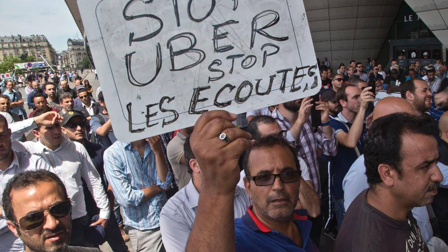 FILE - This Thursday, June 25, 2015 file photo shows a striking taxi driver holding a placard which read, "Stop Uber, Stop listening," referring to the new US spying report in France, during a taxi drivers demonstration in Paris, France. French authorities took two Uber managers into custody for questioning on Monday over "illicit activity" involving its low-cost service. The detentions came amid rising tensions between the government and the ride-hailing company, which culminated last week in a violence-marred taxi strike that blocked roads around the country. (AP Photo/Michel Euler, File)