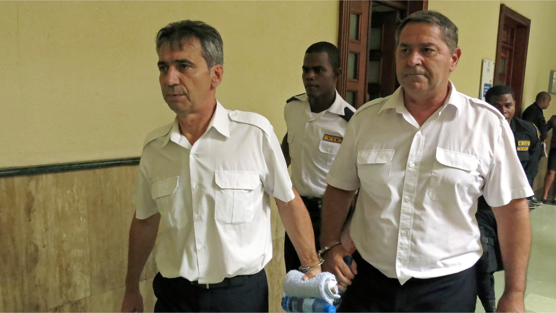 FILE - In this June 17, 2014 file photo, French pilots Bruno Odos, left, and Pascal Jean Fauret, who have been formally charged with drug trafficking, are escorted to a courtroom in Santo Domingo, Dominican Republic. The two French pilots convicted to 20 years in prison for cocaine trafficking fled house arrest and have returned to France, their lawyer says Tuesday, Oct.27, 2015. The French government insisted it didnât have anything to do with the daring and unusual escape. (AP Photo/Ezequiel Abiu Lopez, File)