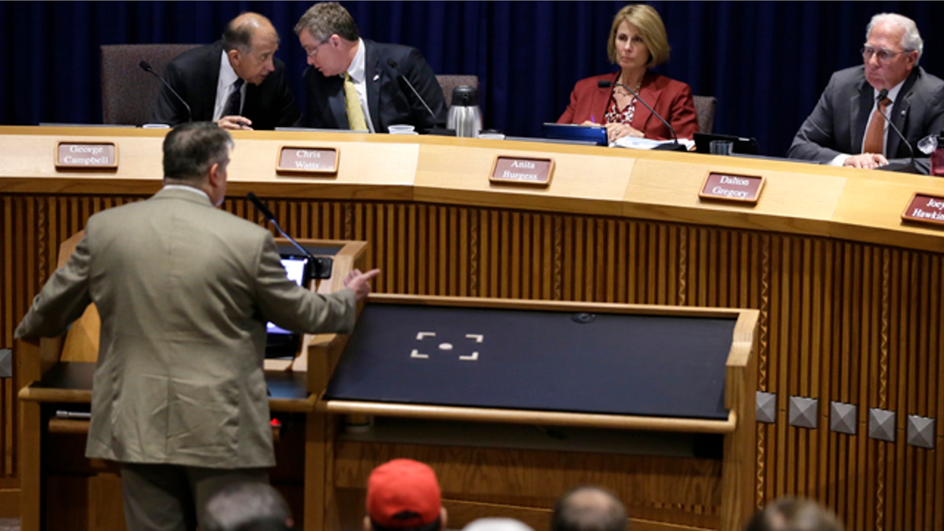 July 15, 2014: Denton, Texas Council member George Campbell, left rear, talks with Mayor Chris Watts as council members Anita Burgess and Dalton Gregory right, listen to former Texas Railroad Commission executive director John Tintara, at lectern, speak at a public hearing at City Hall. (AP Photo/Tony Gutierrez)