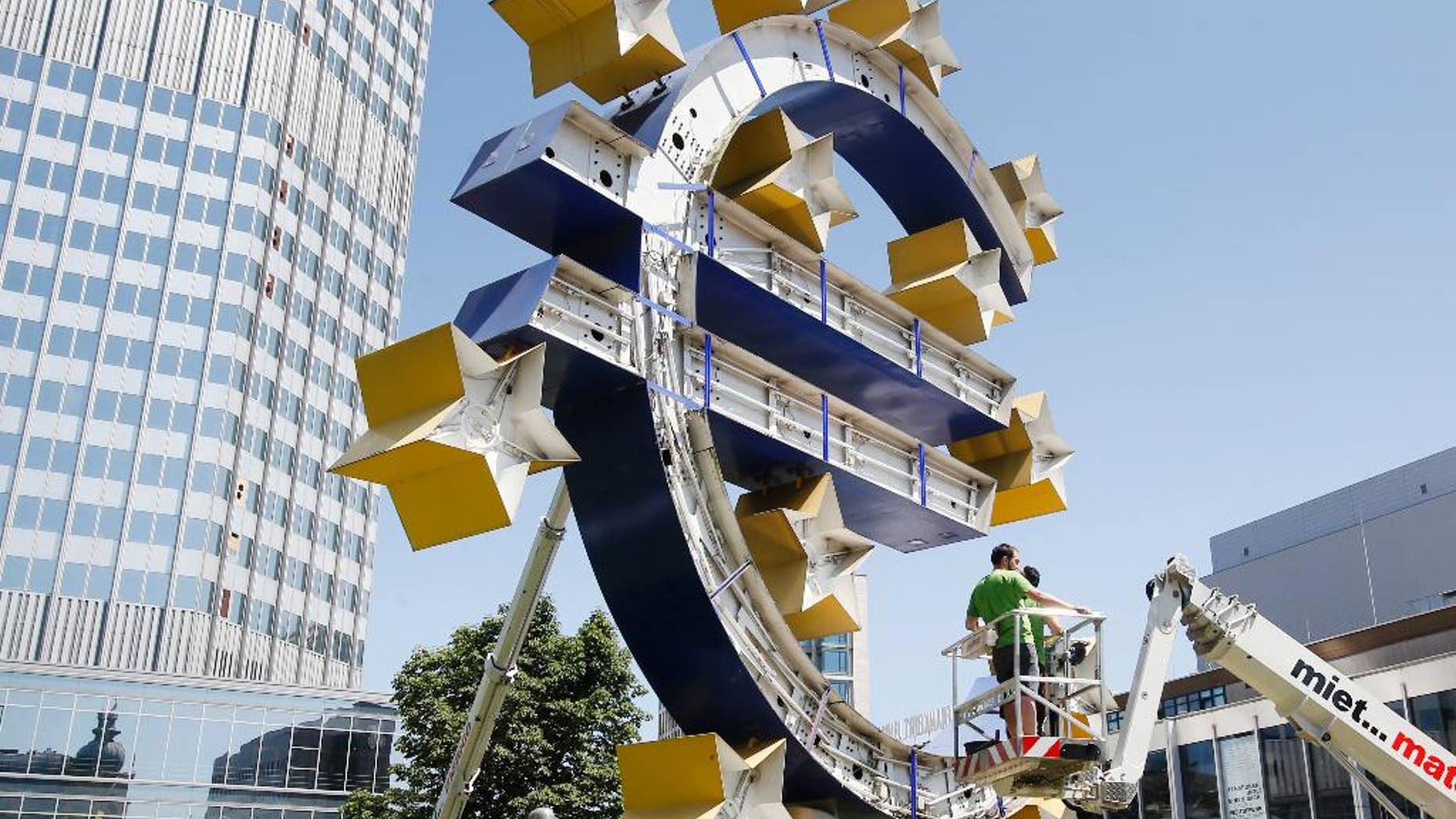 Two workers stand on a lifting platform during renovation works at the Euro sculpture in front of the old European Central Bank in Frankfurt, Germany, Monday, July 6, 2015. The sculpture will be renovated during the next four days. (AP Photo/Michael Probst)