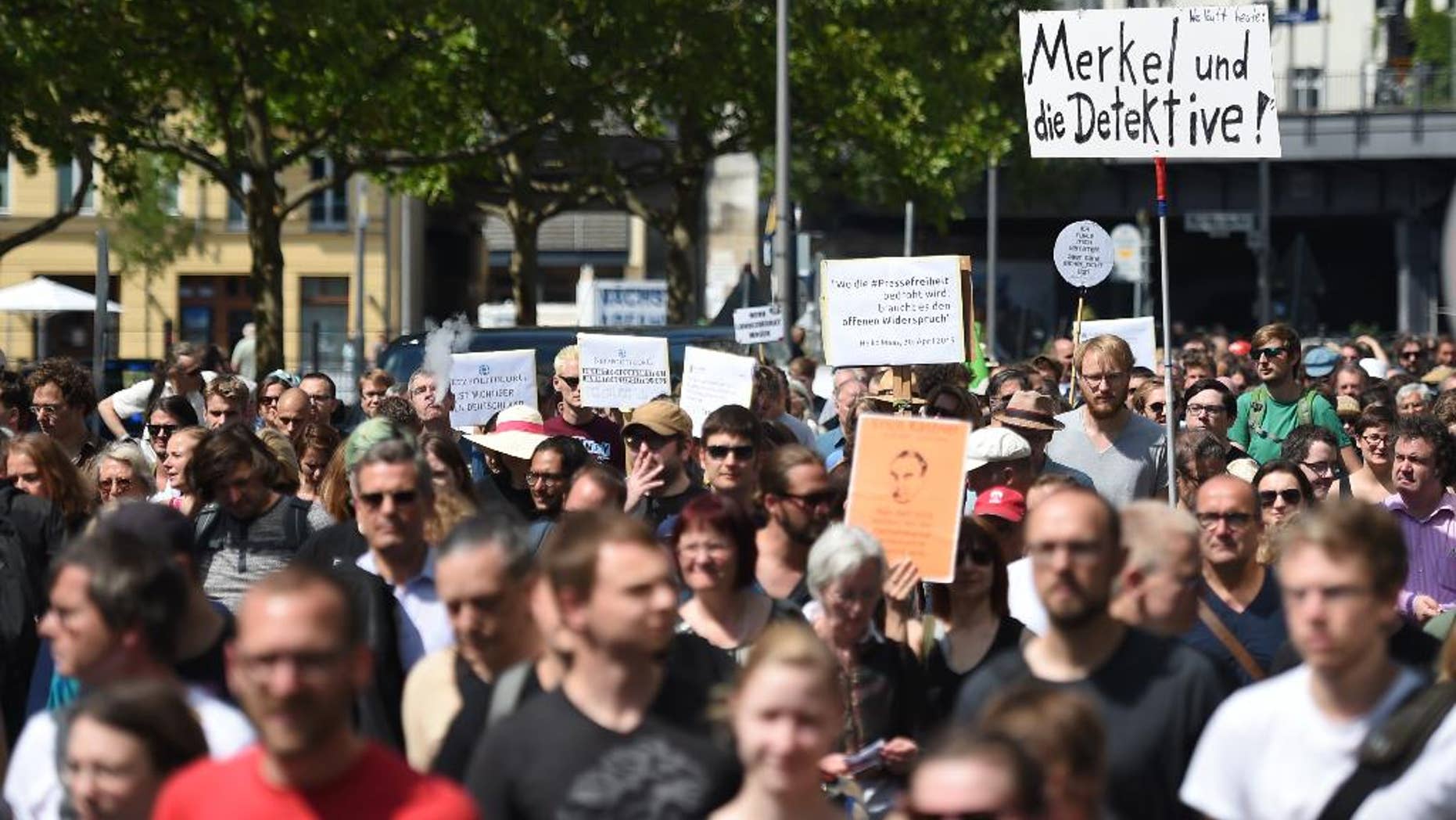 Participants of a demonstration protest in Berlin, Saturday Aug. 1, 2015. Banner at right reads "Merkel und die Detektive!" (lt: Merkel and the detectives). Some 1,300 people rallied in Berlin for the freedom of the press in support of two journalists who prosecutors are investigating for treason over two reports revealing authorities' plans to expand surveillance of online communication. Website Netzpolitik.org, which covers digital rights issues, said Thursday it was notified by federal prosecutors of the probe against its staff and an unidentified source over the two reports. (Britta Pedersen/dpa via AP)