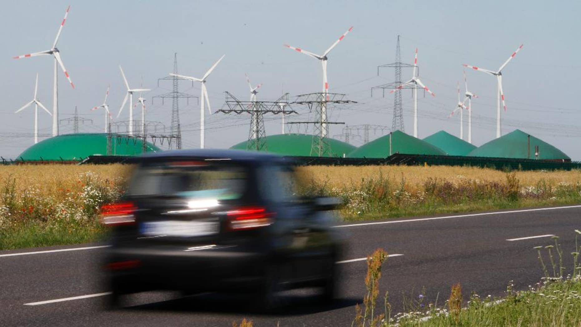 FILE - In this June 29, 2011 file photo a car passes by a a biogas plant and windmills near Nauen, Germany. The crisis in Ukraine is underlining the urgency of Germany's biggest political challenge as Chancellor Angela Merkel's new government marks 100 days in office Wednesday, March 26, 2014, getting the country's mammoth transition from nuclear to renewable energy sources on track. The transition started in earnest when Merkel, after Japan's 2011 Fukushima nuclear disaster, abruptly accelerated Germany's exit from nuclear power. Since then, the "Energiewende" _ roughly, "energy turnaround" _ has created increasing headaches. (AP Photo/Ferdinand Ostrop, File)