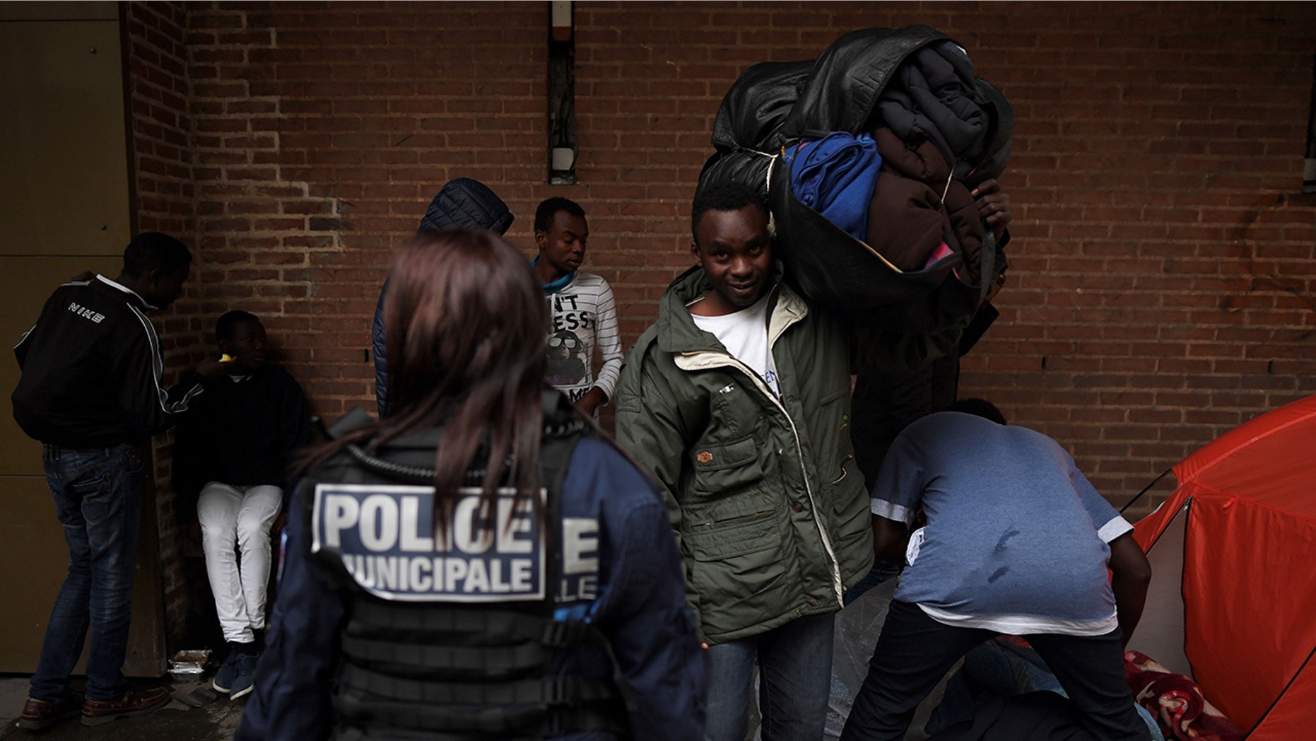 A police officer stands guard as migrants pack up their belongings after sleeping on the floor in Saint-Denis outside Paris on October 11, 2017.